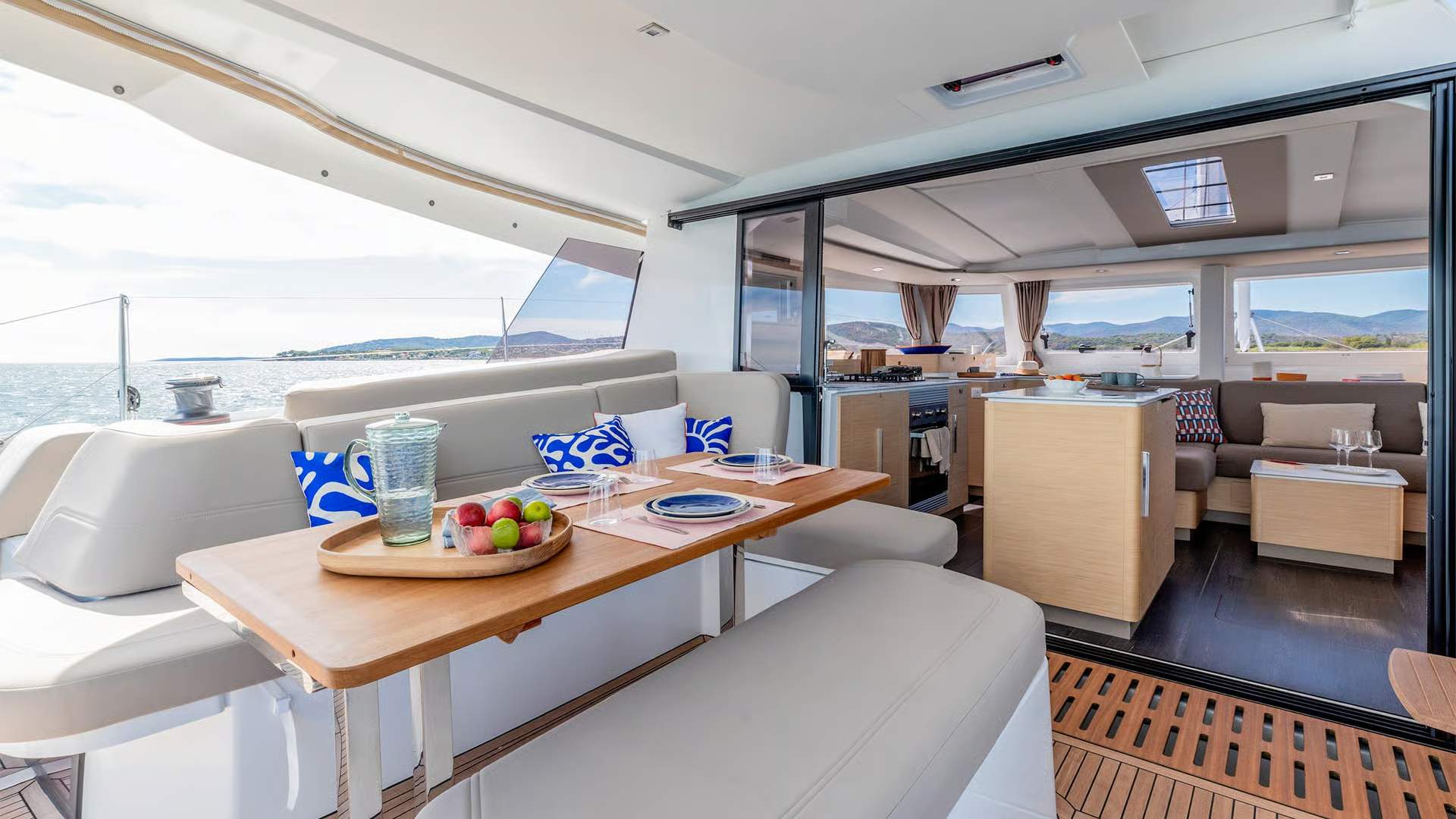 View of the spacious aft cockpit aboard the Fountaine Pajot FP44 catamaran with a dining area and open access to the saloon.