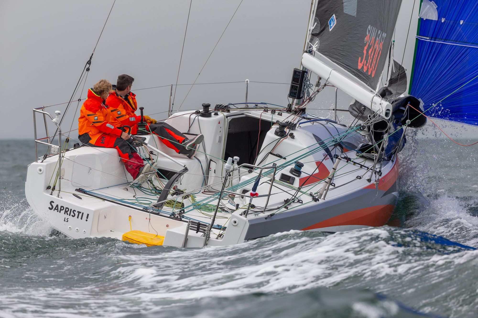 Zwei Personen in oranger Regattabekleidung an Bord der Jeanneau Sun Fast 3300 während einer Regatta.