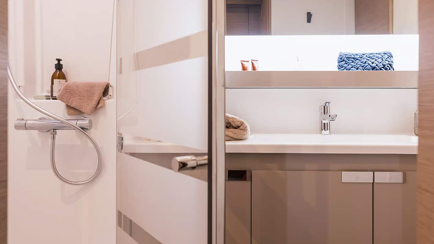 Innenraum eines Bades an Bord des Katamarans Fountaine Pajot Aura 51, mit sichtbarer Dusche und Waschbecken mit Spiegel.