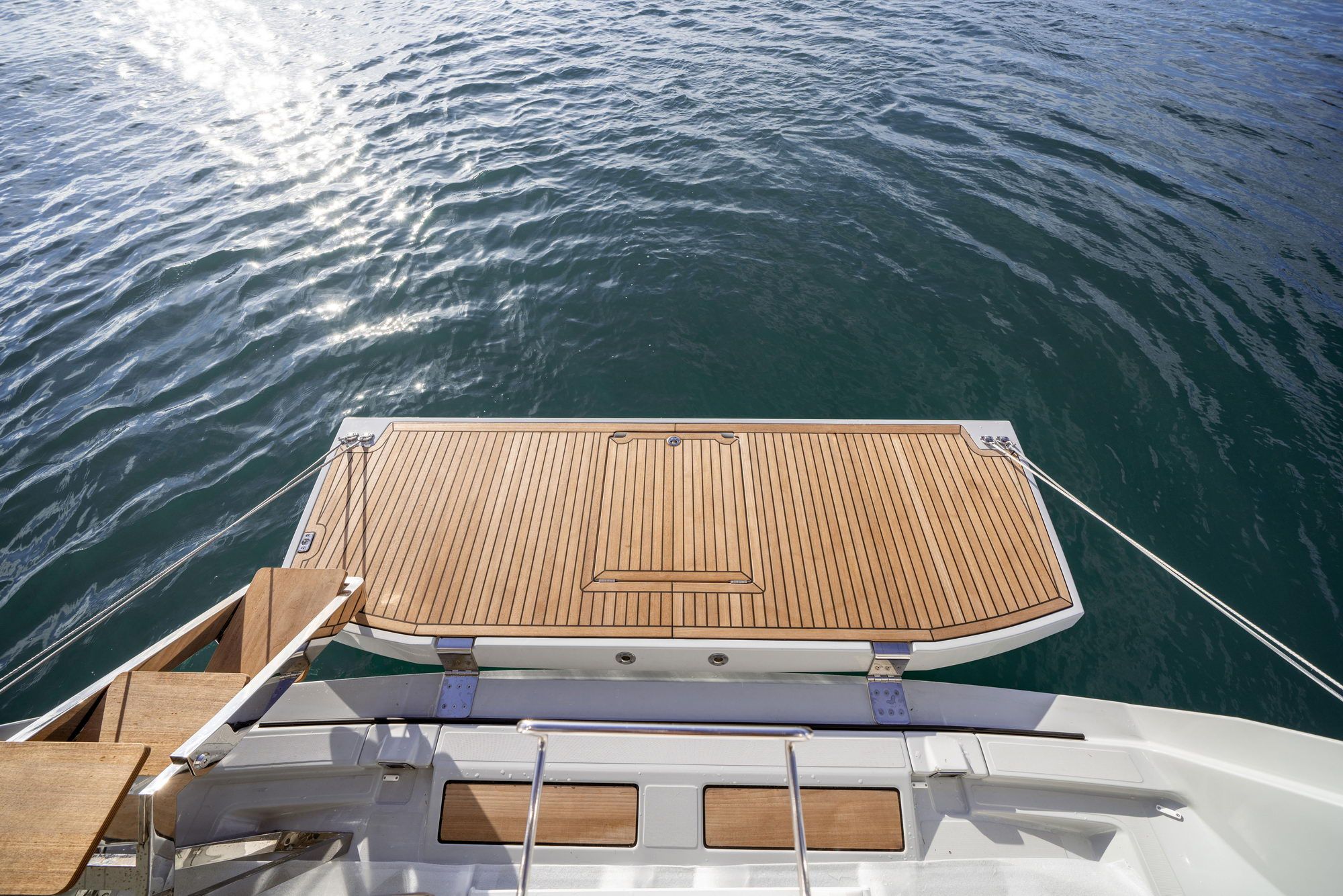 Widok z góry na otwartą, drewnianą platformę kąpielową na rufie jachtu Jeanneau Yachts 65, z wodą w tle.