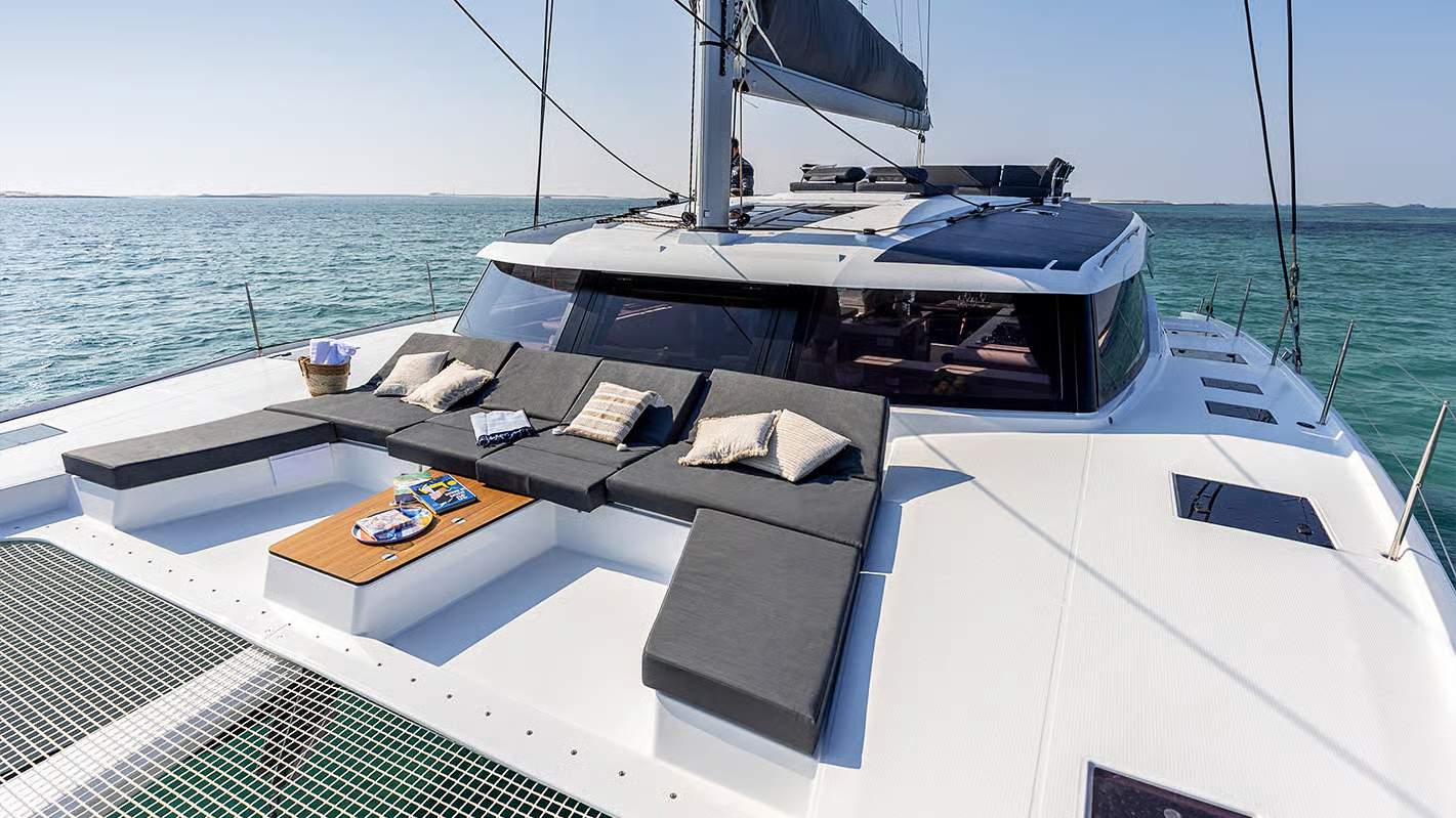 View of the spacious foredeck of the Fountaine Pajot Aura 51 catamaran with comfortable sofas and a table, with the sea in the background.
