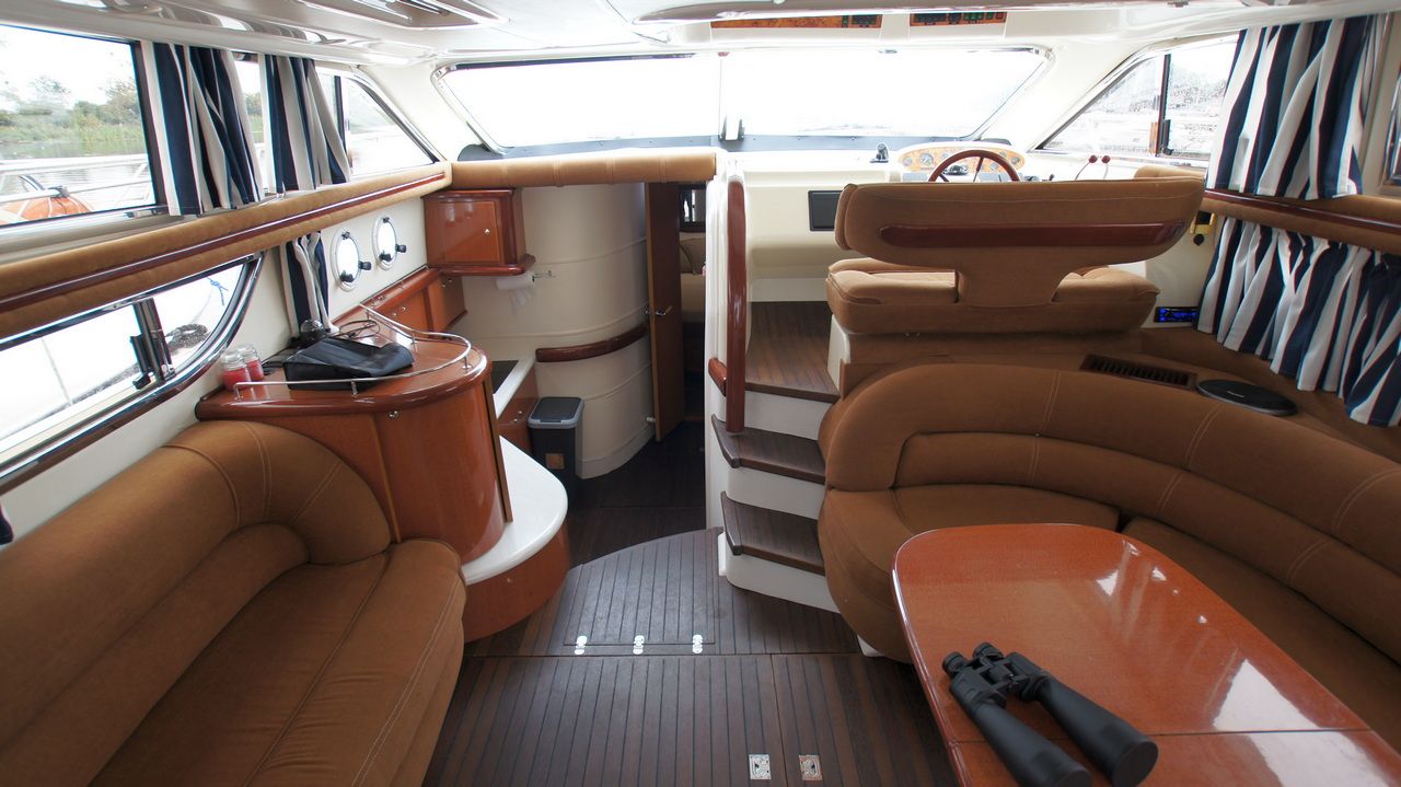 Widok na przestronny salon i sterówkę jachtu motorowego Sealine F44 Flybridge z brązowymi sofami i drewnianymi elementami.