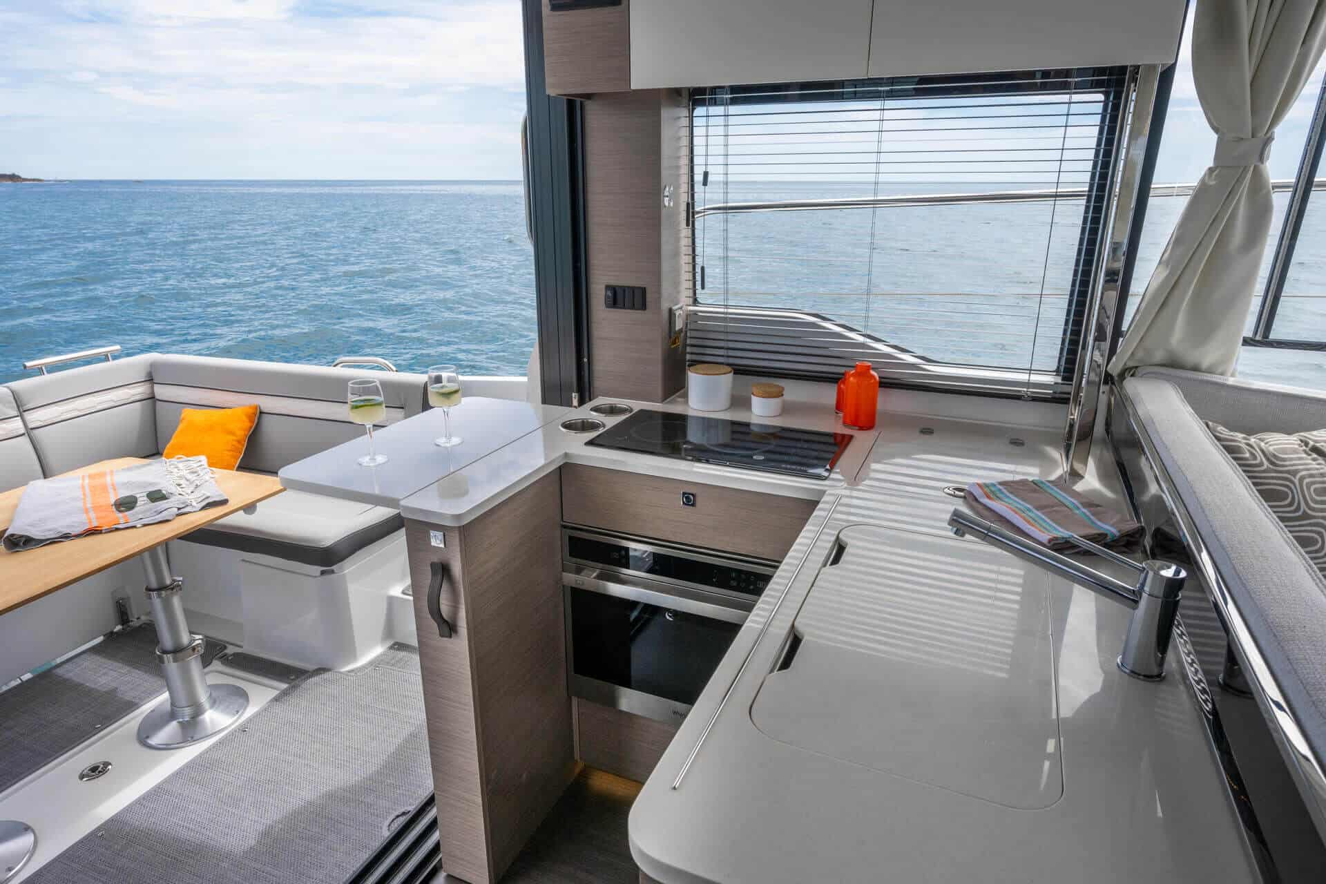 Nowoczesna kuchnia z piekarnikiem i płytą grzewczą oraz salon z sofą i stołem na jachcie Jeanneau Merry Fisher 1295 Flybridge z widokiem na morze.