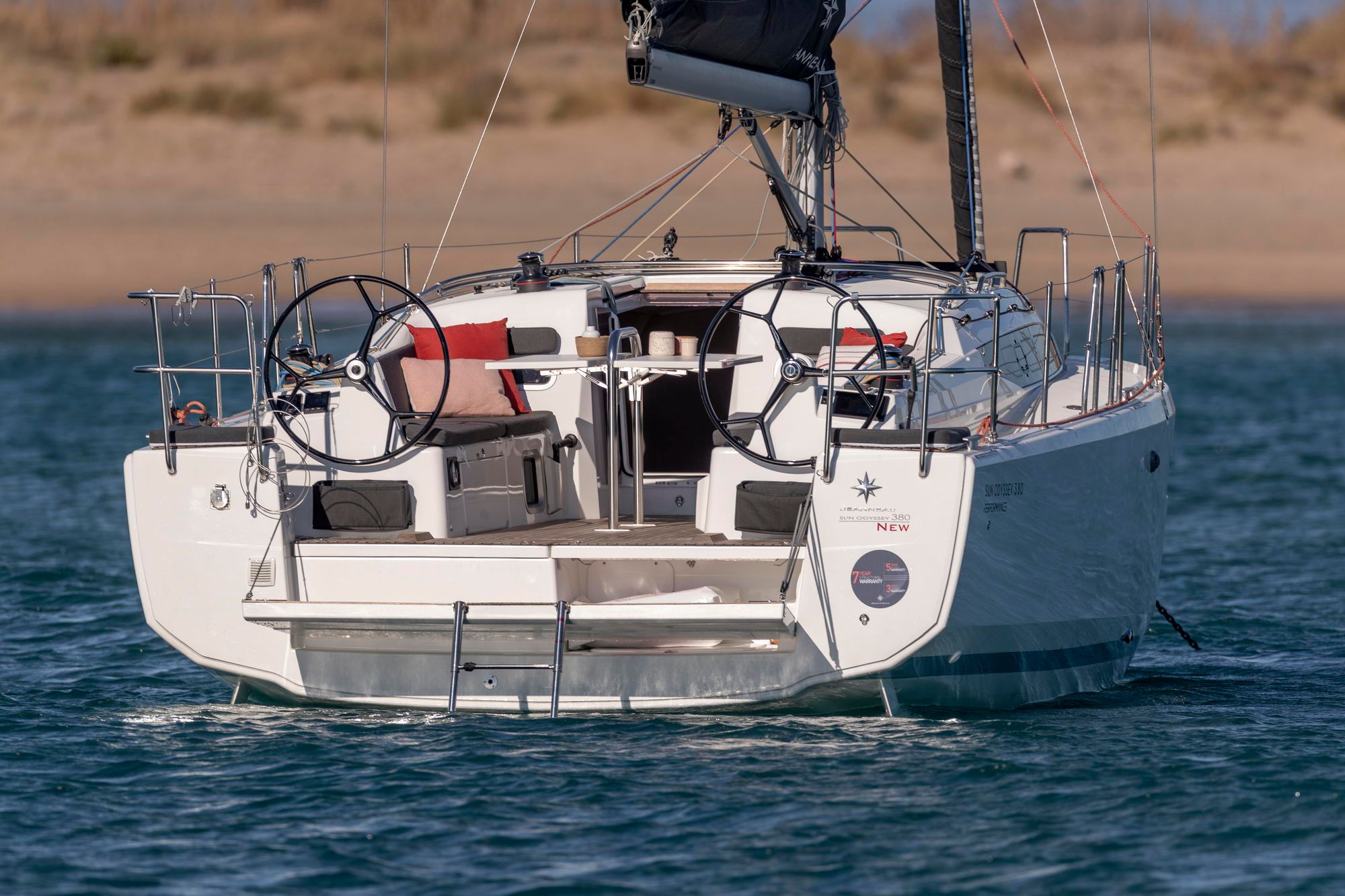 Widok z tyłu na jacht żaglowy Jeanneau Sun Odyssey 380 na wodzie. Widoczne podwójne koła sterowe, kokpit i platforma kąpielowa.
