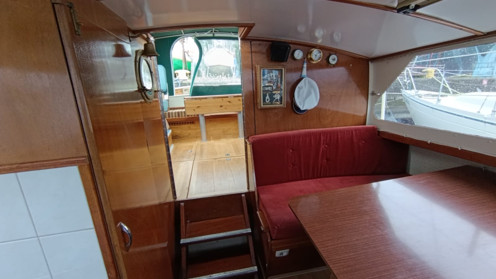 Innenraum der Motoryacht Aquanaut 750 mit rotem Sofa, Holztisch und Zugang zum Cockpit.