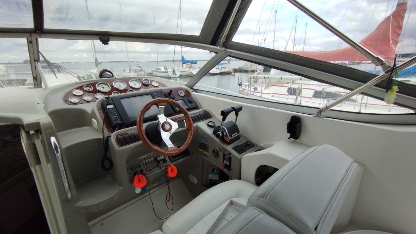 View of the Bayliner 3055 helm station with a steering wheel, gauge panel and Simrad chartplotter. A marina is visible in the background.