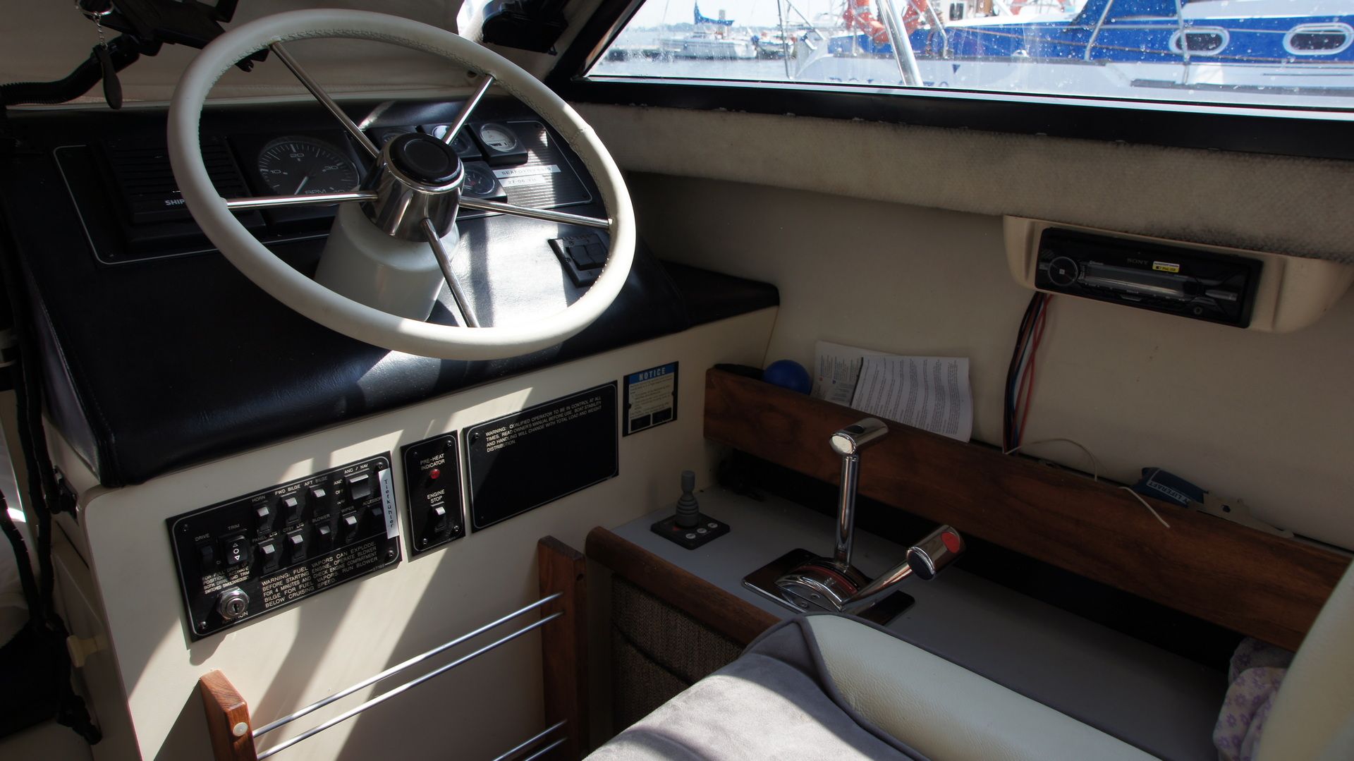 Widok na wewnętrzne stanowisko sterowe łodzi Bayliner 2858 Classic Fly z kierownicą, panelami kontrolnymi i manetką.