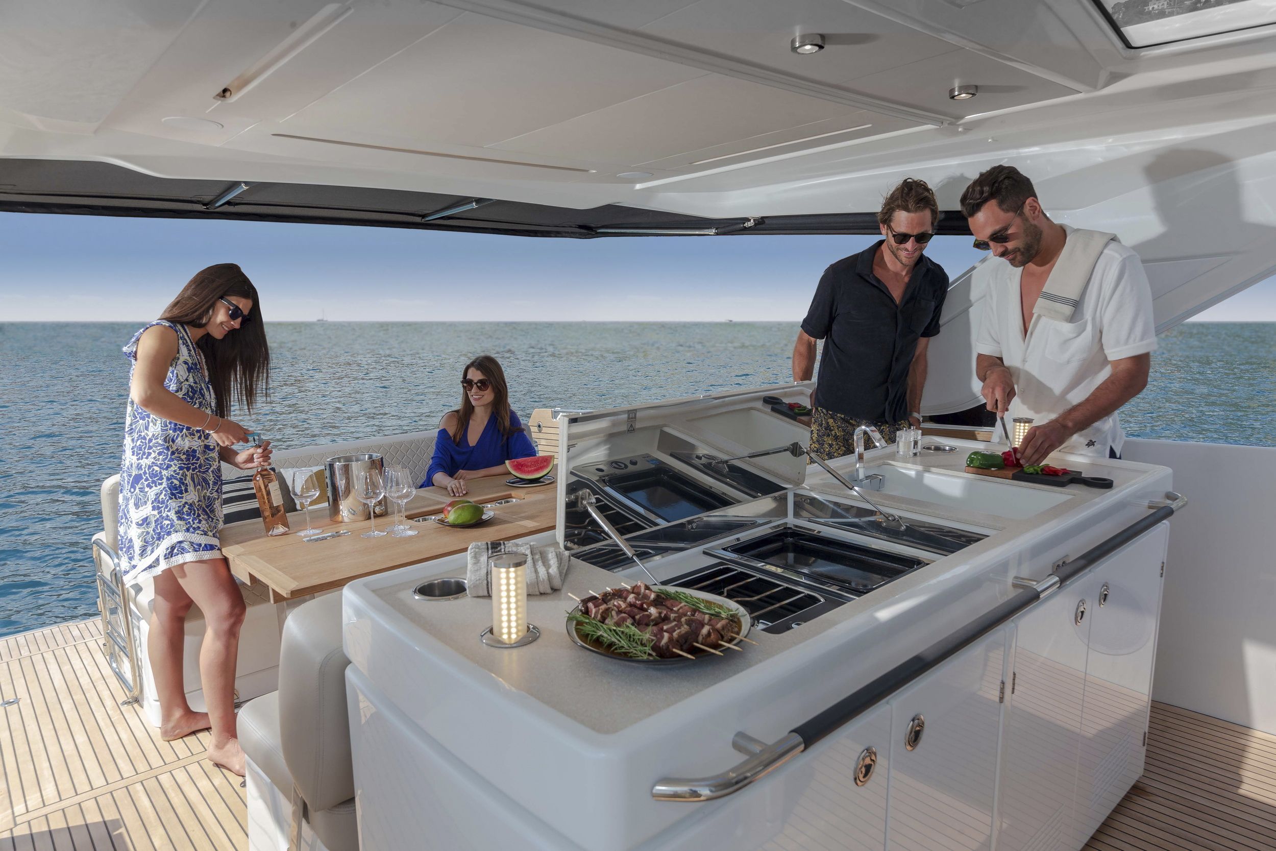 Four people in the cockpit of the Jeanneau DB/43 IB. The on-board galley, table and sofa are visible. People preparing a meal and relaxing.