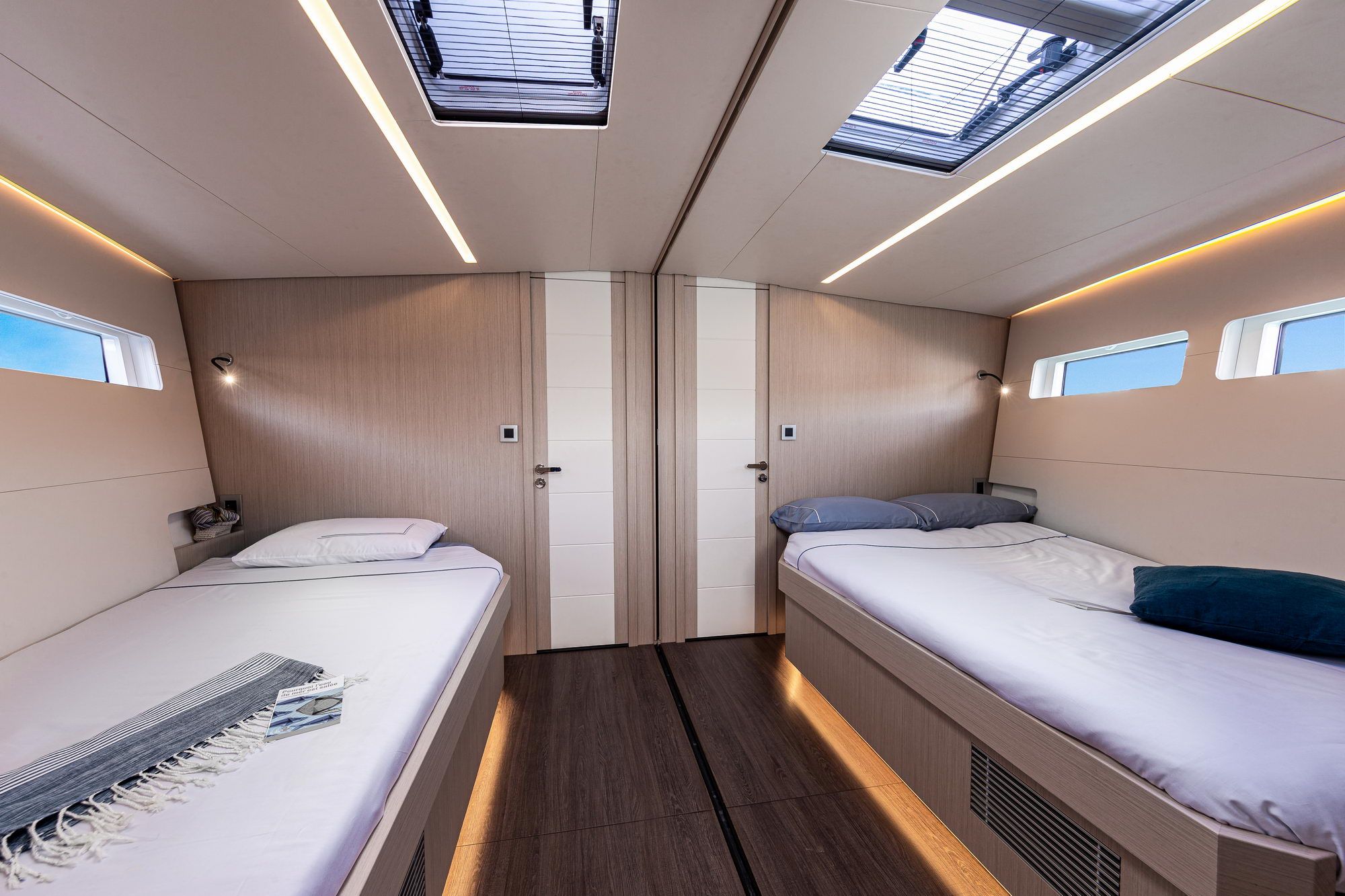 Wnętrze kabiny gościnnej jachtu Jeanneau Yachts 60 z dwoma pojedynczymi łóżkami, oknami i oświetleniem LED.