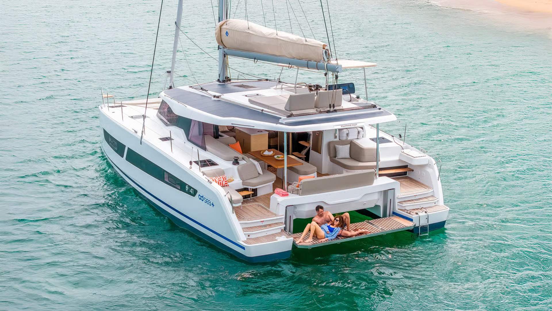 Widok z lotu ptaka na rufę katamaranu Fountaine Pajot FP41 z dwoma osobami relaksującymi się na zintegrowanym leżaku. Widoczne są również kokpit i pokład słonec