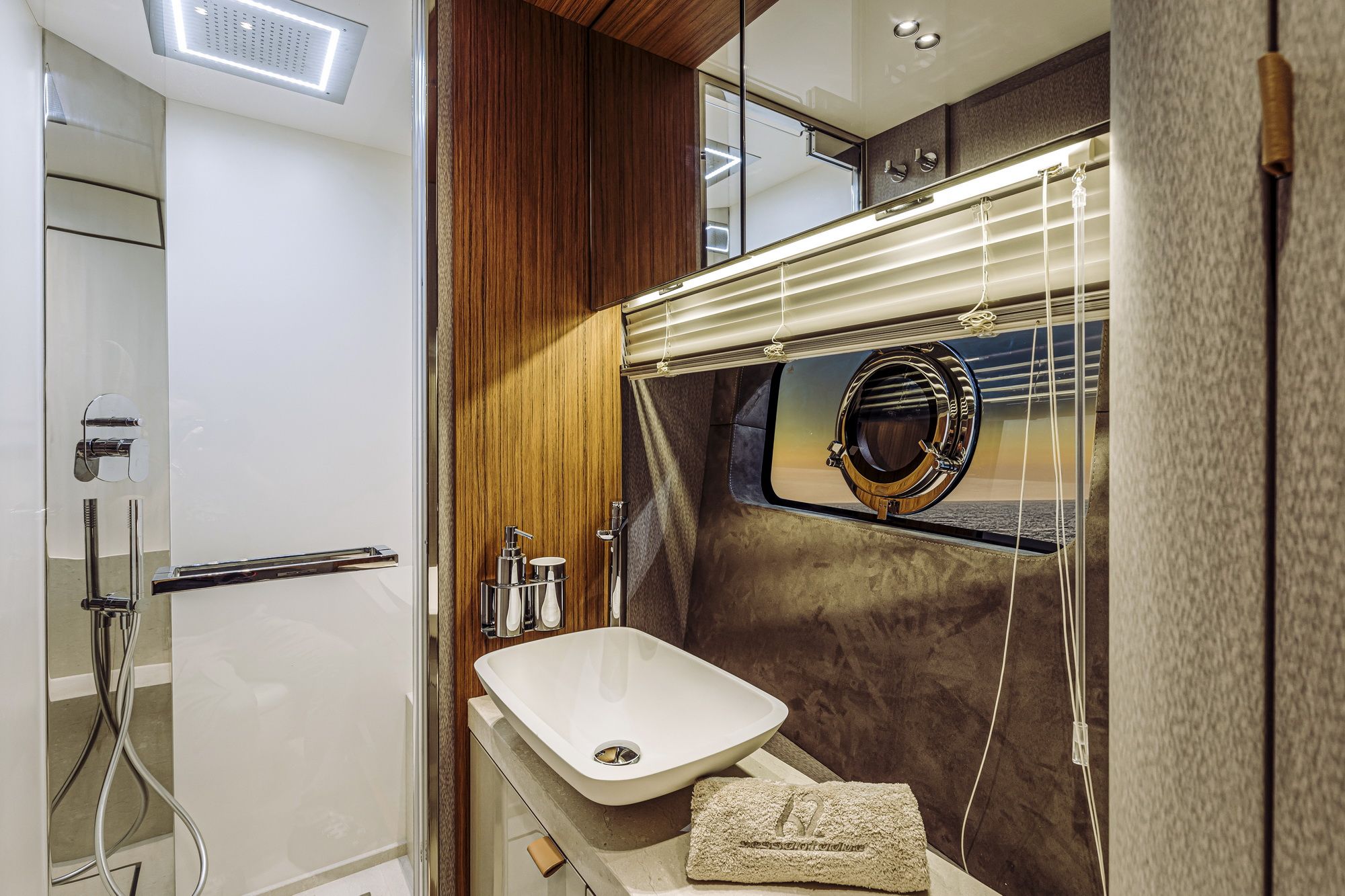Modernes Badezimmer an Bord der Cranchi Sessantadue 62 mit Dusche, Waschbecken und rundem Bullauge mit Meerblick.