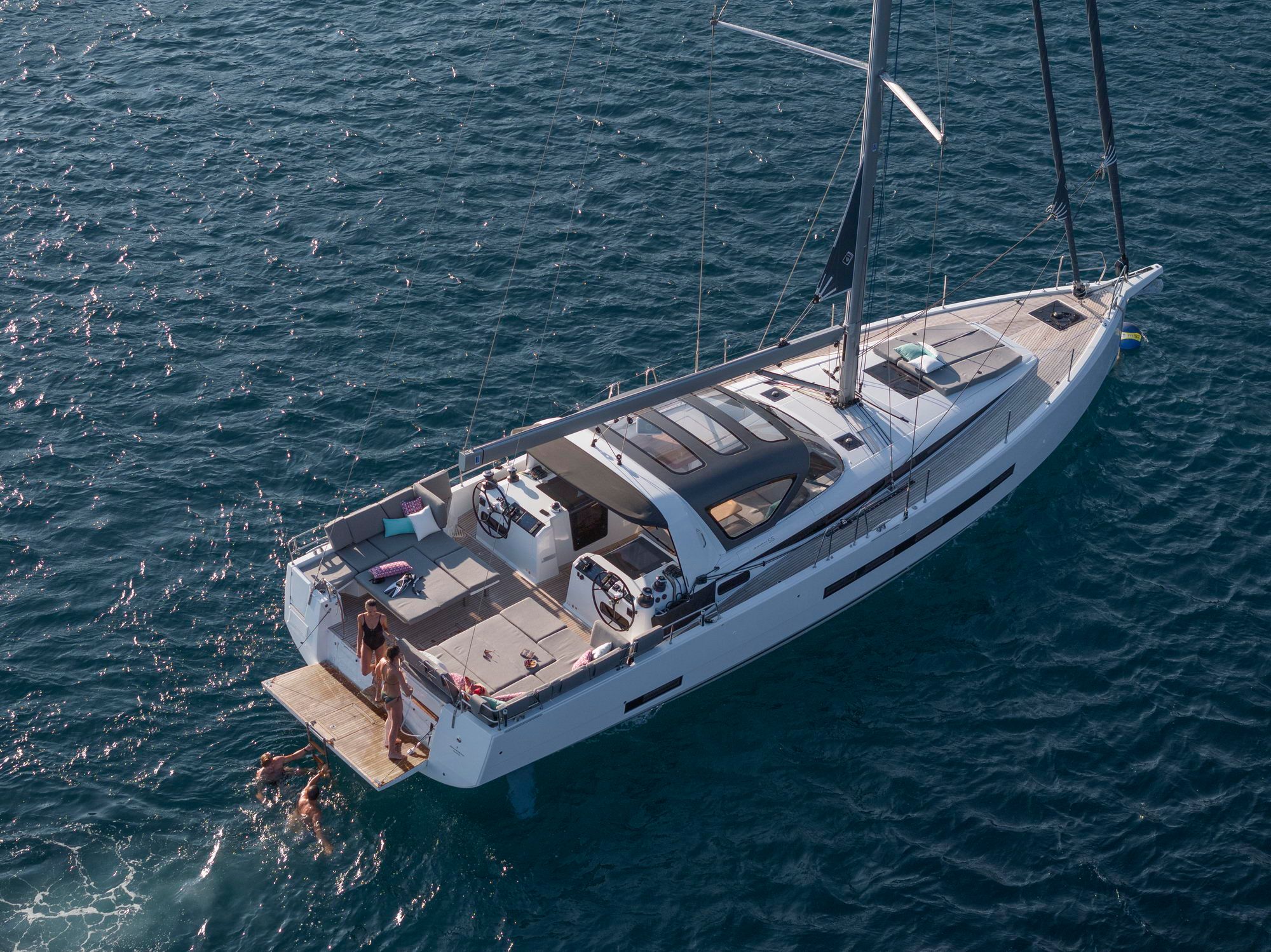 Widok z lotu ptaka na jacht żaglowy Jeanneau Yachts 55 z opuszczoną platformą kąpielową i ludźmi w wodzie.
