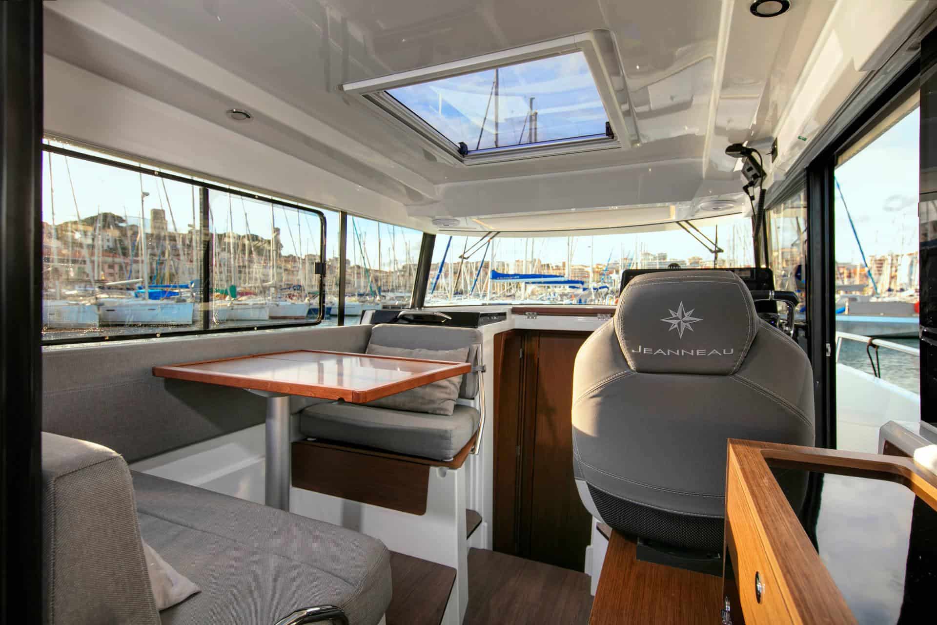 Wnętrze Jeanneau Merry Fisher 895 Sport S2 z widokiem na stół, kanapy i fotel sternika w marinie.