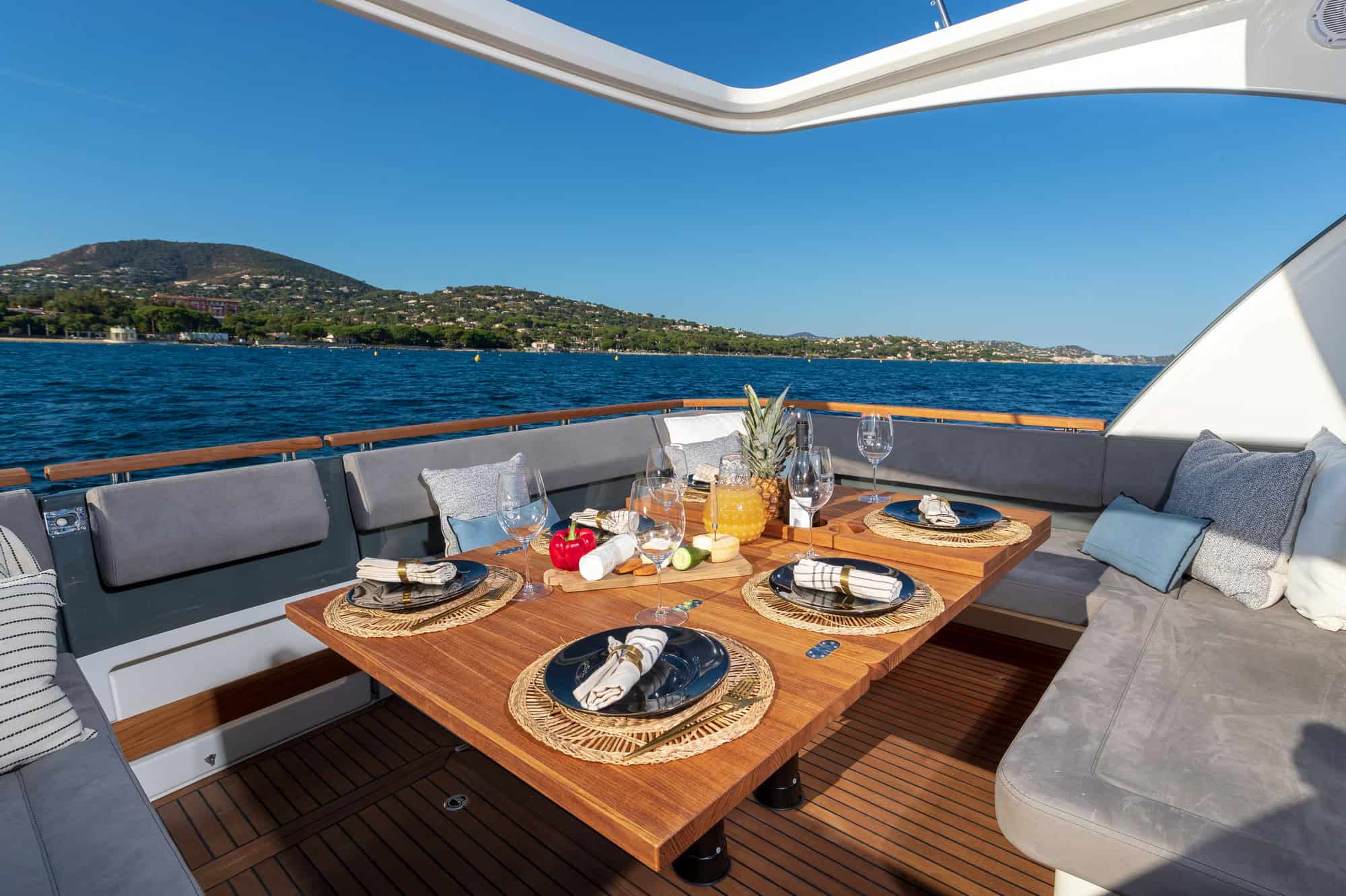 Zastawiony stół z drewna tekowego w kokpicie jachtu Marex 440 Gourmet Cruiser, z widokiem na morze i wybrzeże.