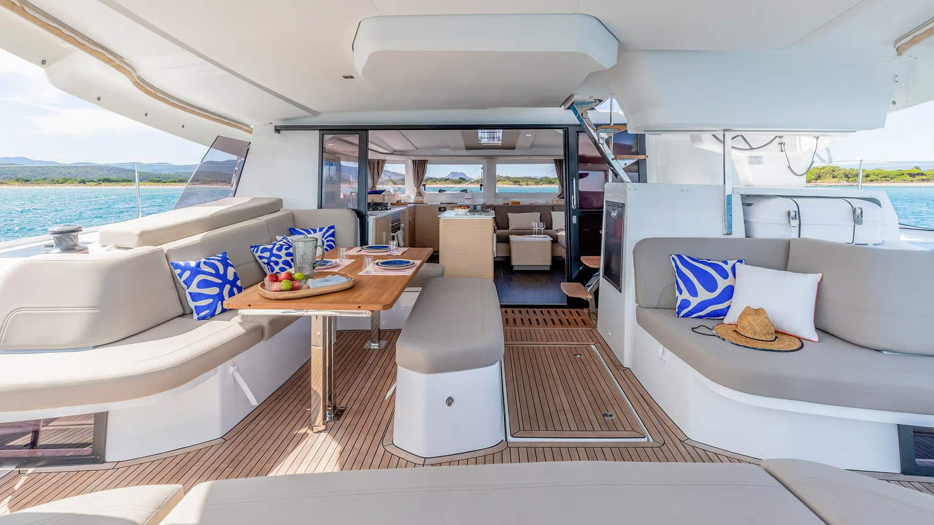 Spacious aft cockpit aboard the Fountaine Pajot FP44 catamaran with a dining area, sofas and sea views.