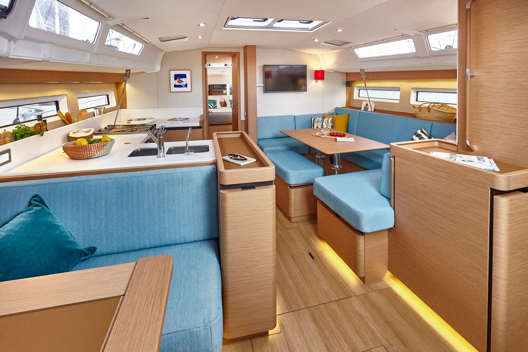 Wnętrze jachtu Jeanneau Sun Odyssey 490. Widoczny przestronny salon z jasnoniebieskimi kanapami, stołem i telewizorem oraz w pełni wyposażony kambuz.