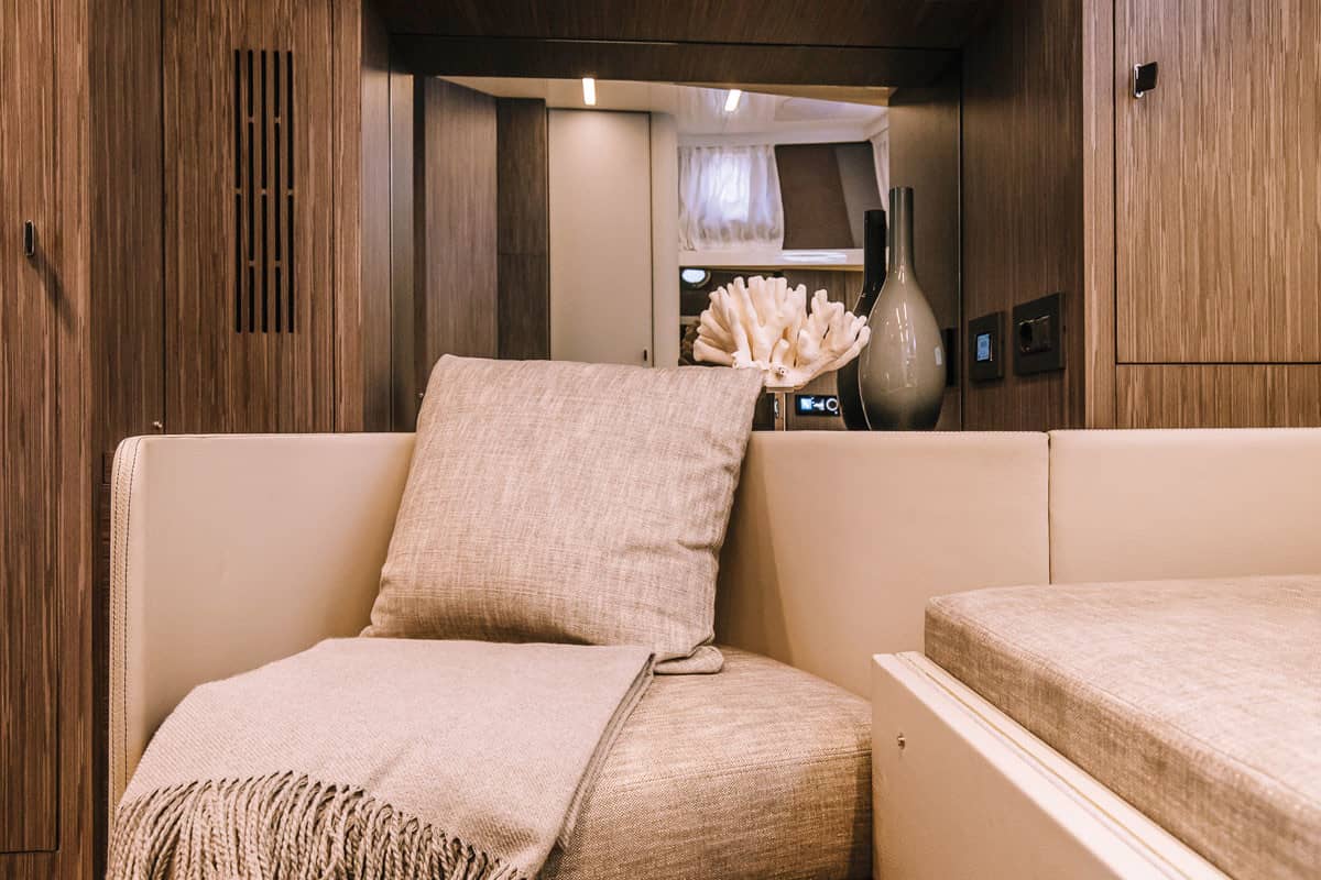 Wnętrze kabiny jachtu Cranchi A46 Luxury Tender z beżową sofą, poduszką, kocem i drewnianymi panelami ściennymi.