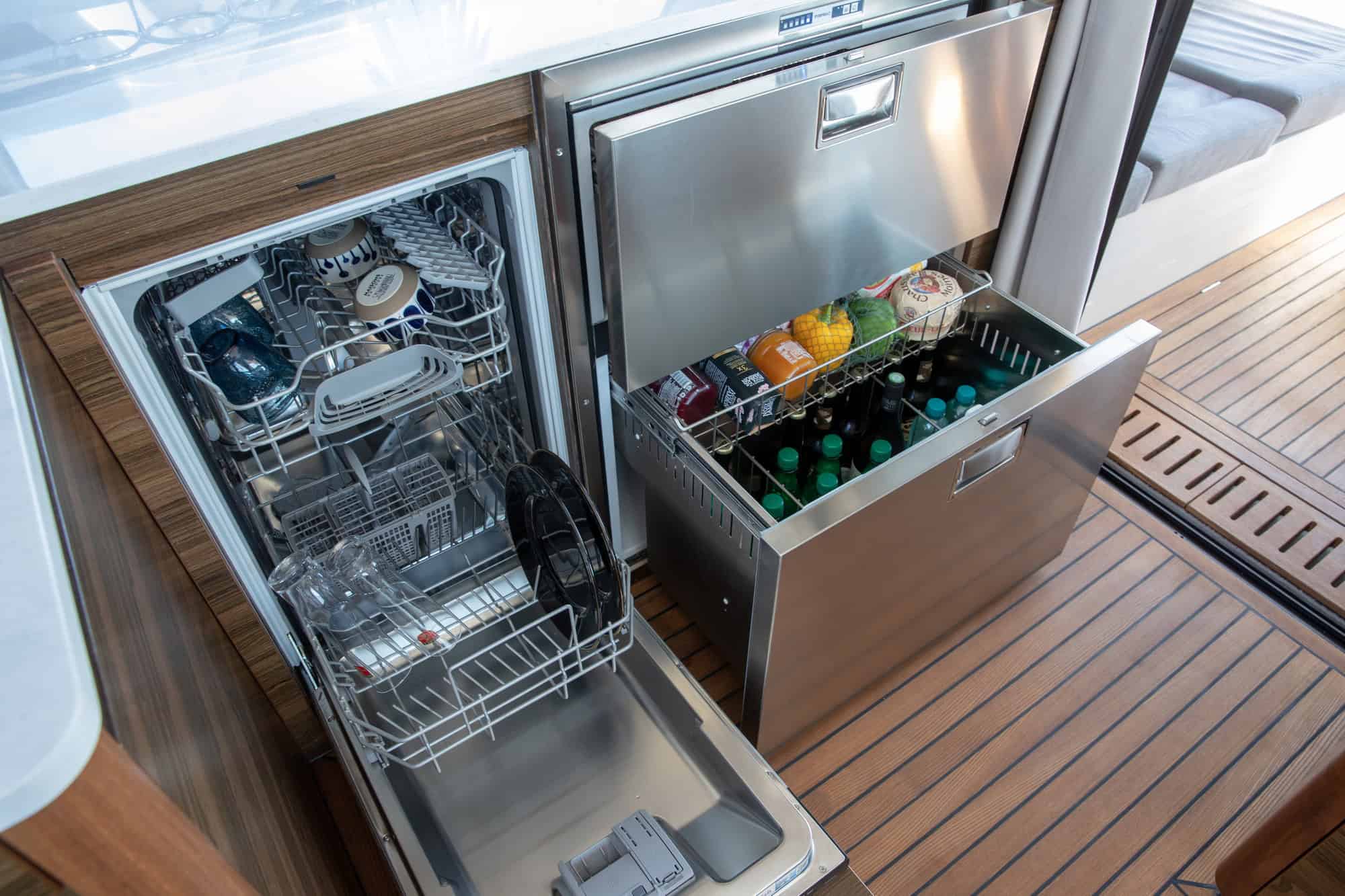 Integrated dishwasher and stainless-steel drawer fridge in the galley of the Marex 440 Gourmet Cruiser. Drinks and vegetables are visible.