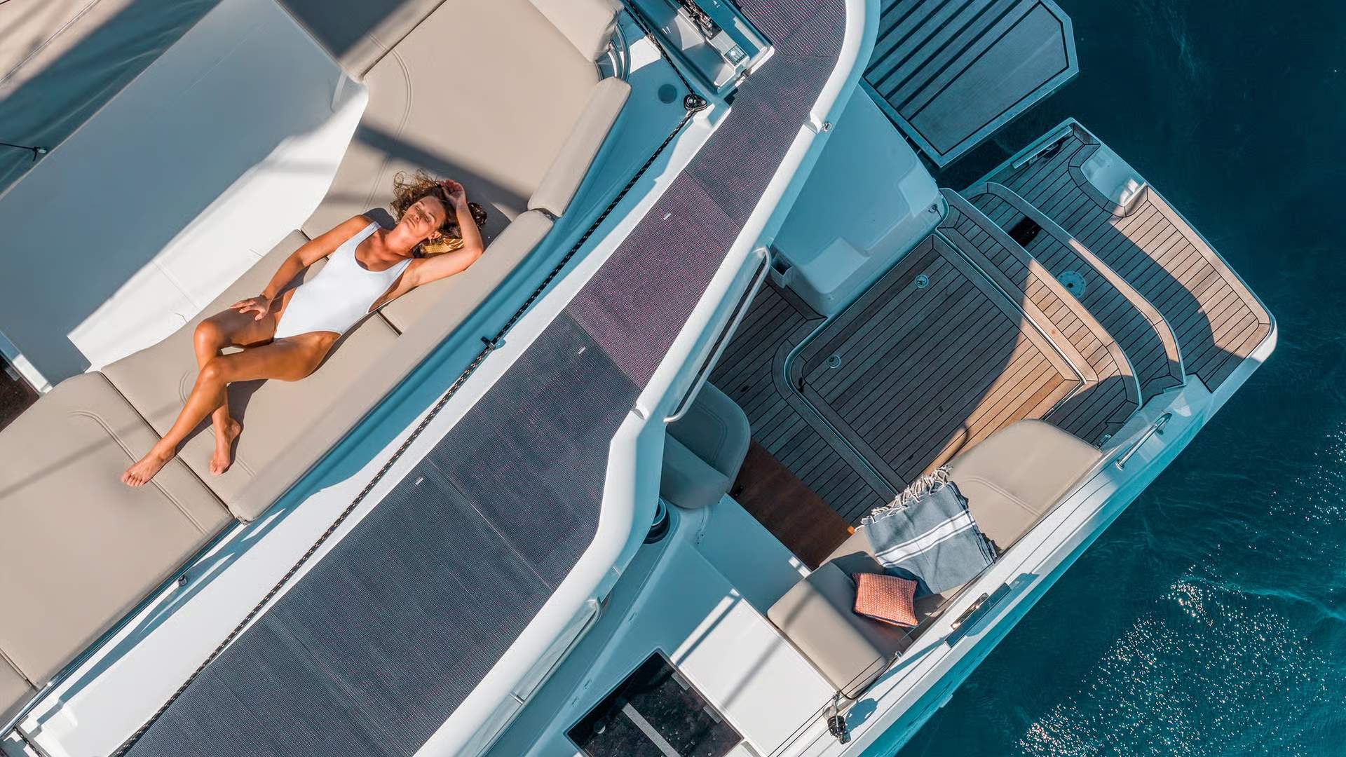Widok z góry na pokład słoneczny katamaranu Fountaine Pajot FP44 z leżącą kobietą i platformą kąpielową.