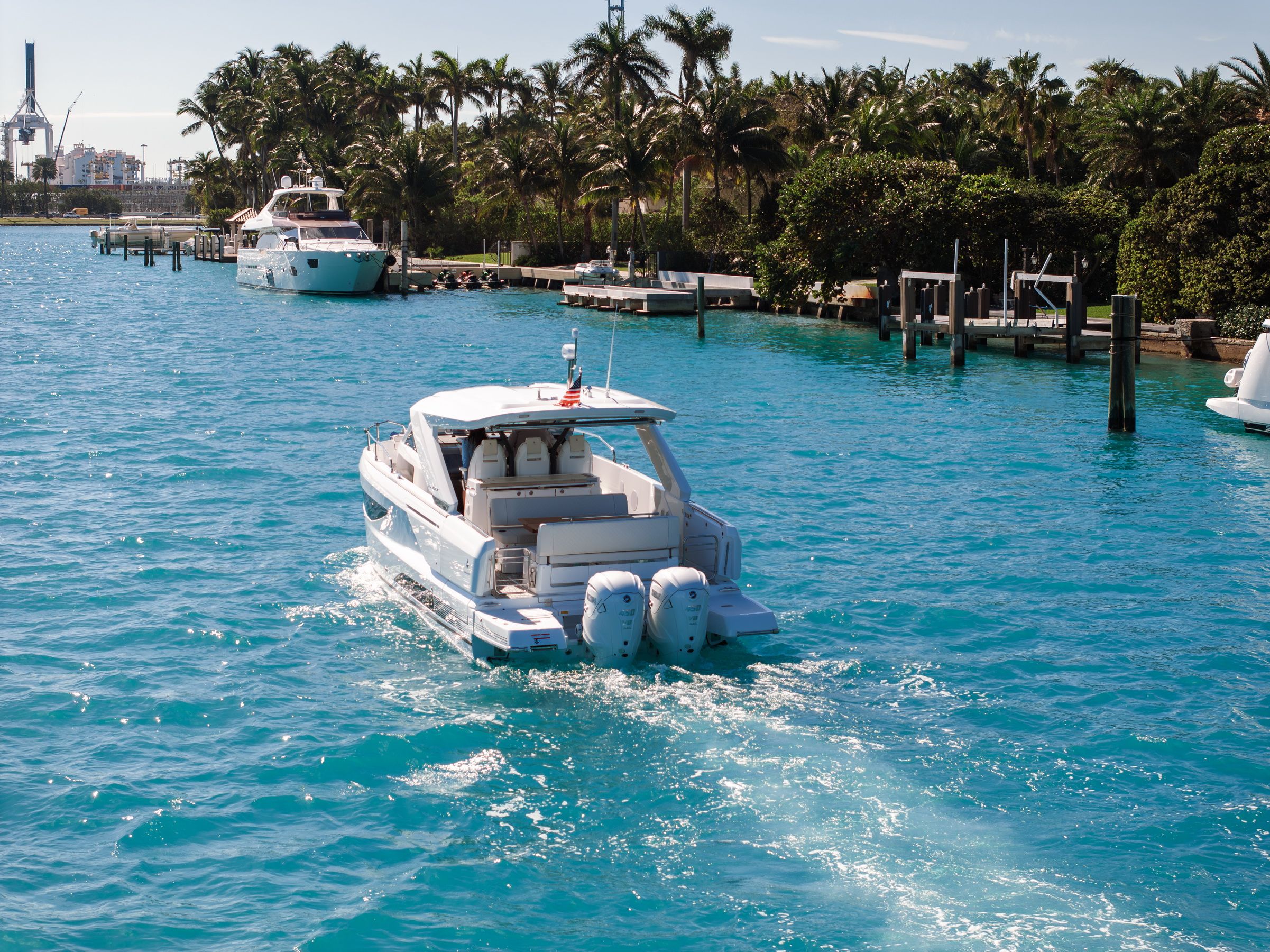 Rear view of the Jeanneau DB/37 OB motorboat with three outboard engines, cruising on blue water, with the open cockpit visible.