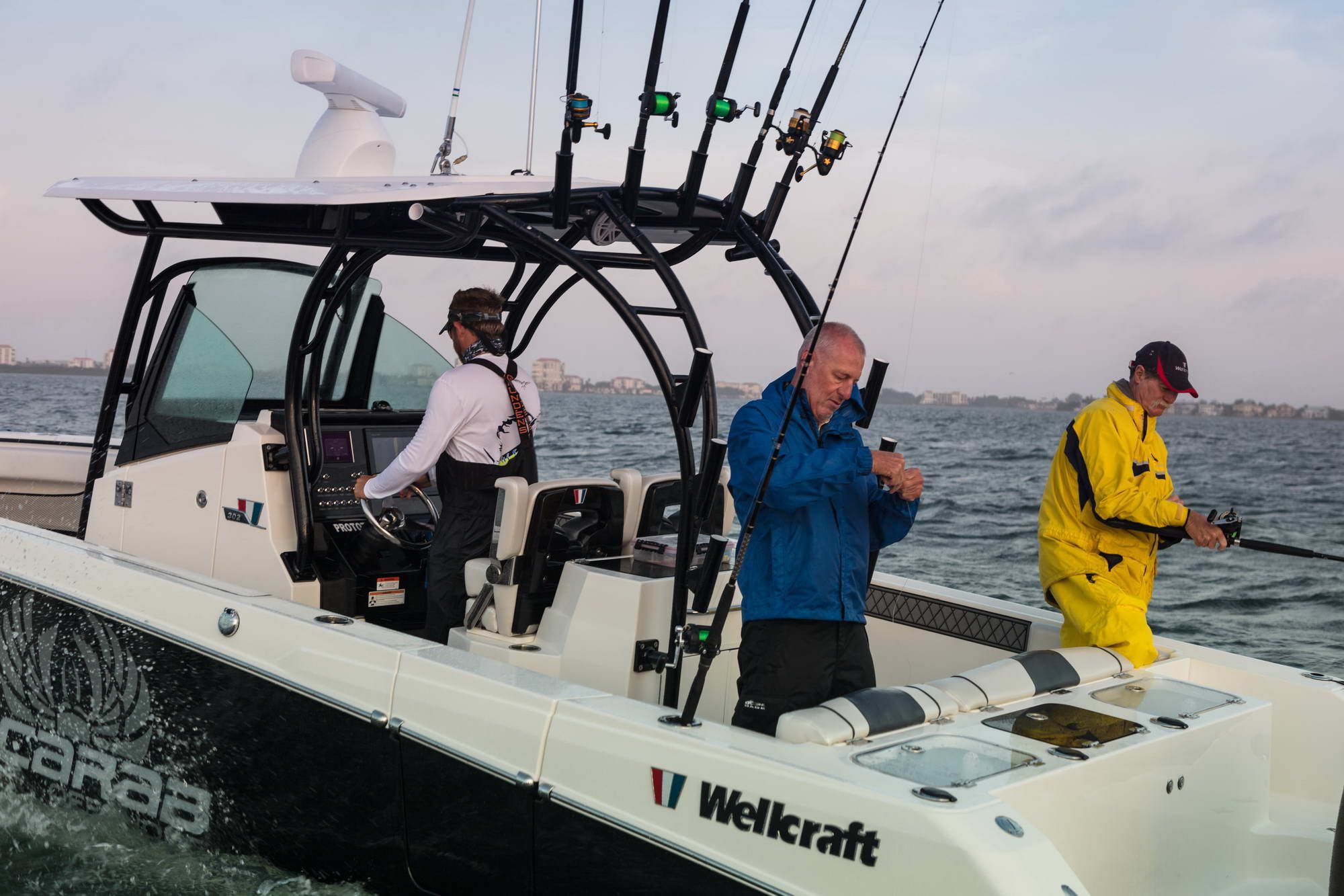 Trzech mężczyzn łowi ryby z pokładu łodzi Wellcraft Fisherman 302 na otwartym morzu. Jeden steruje, dwóch wędkuje.
