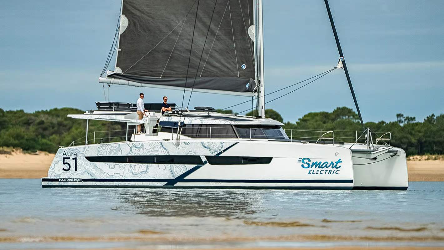 Katamaran żaglowy Fountaine Pajot Aura 51 Smart Electric płynący po wodzie z dwoma osobami na pokładzie.