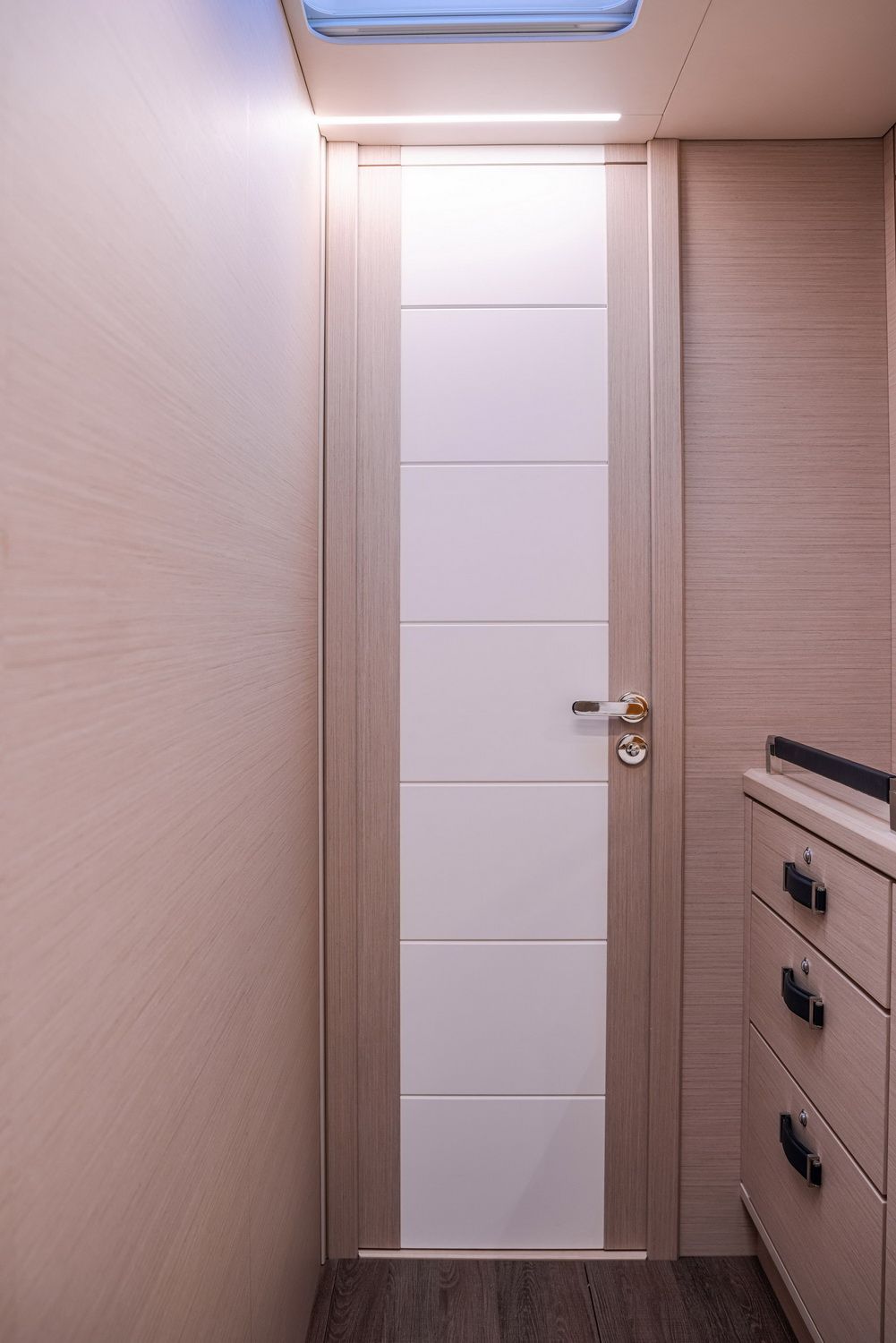 Moderne Innentüren mit hellem Holzfinish und weißen Paneelen, daneben eine Schubladenkommode in der Kabine der Yacht.