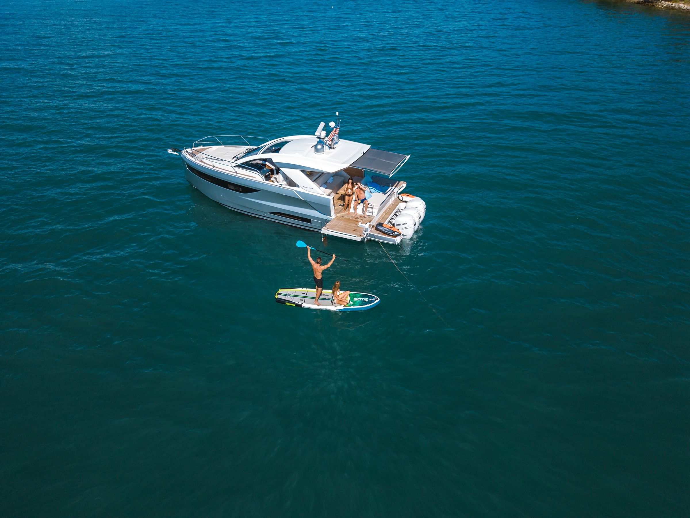 Luftaufnahme der Jeanneau DB/43 OB mit Personen an Bord und auf einem Paddleboard, auf offener See.