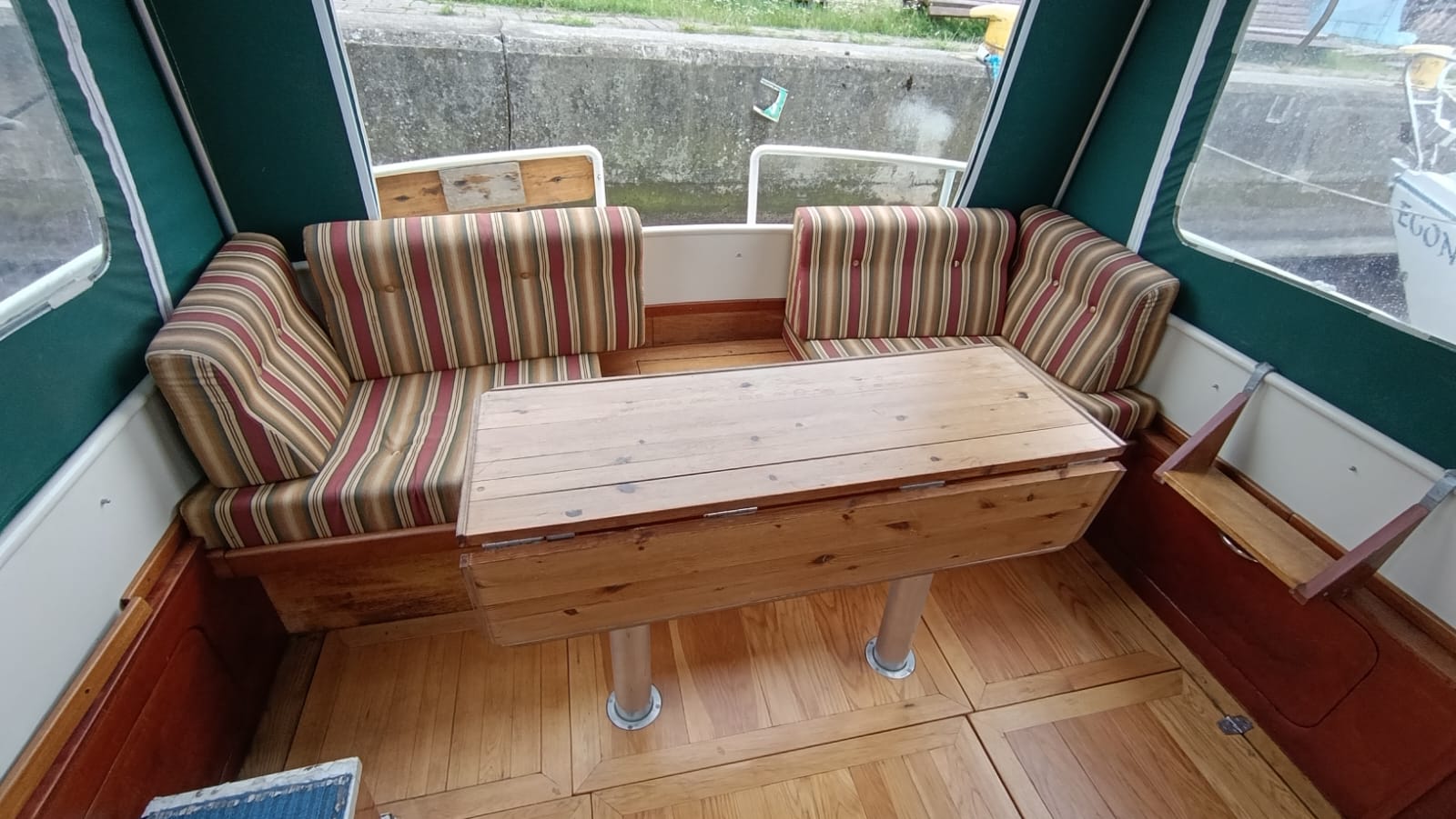 Interior of the Aquanaut 750 cockpit with a wooden table and sofas with striped cushions, under a green canopy.