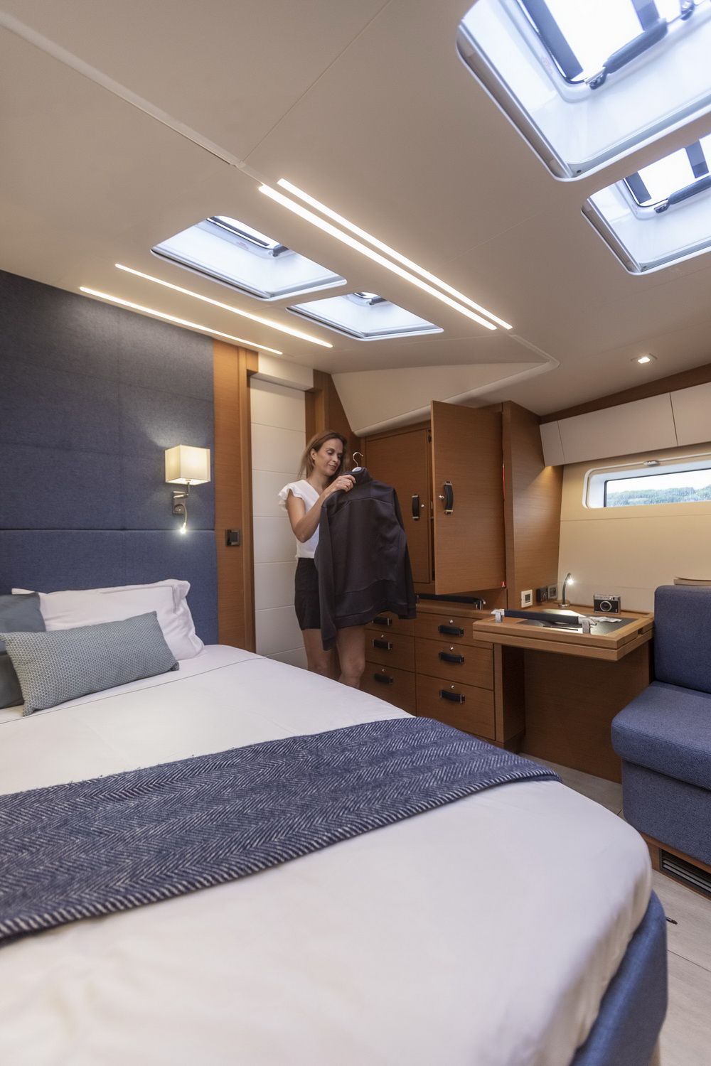 Eine Frau in der Eignerkabine der Jeanneau Yachts 65, beim Aufhängen von Kleidung im Schrank. Ein großes Schlafzimmer mit Dachfenstern ist sichtbar.
