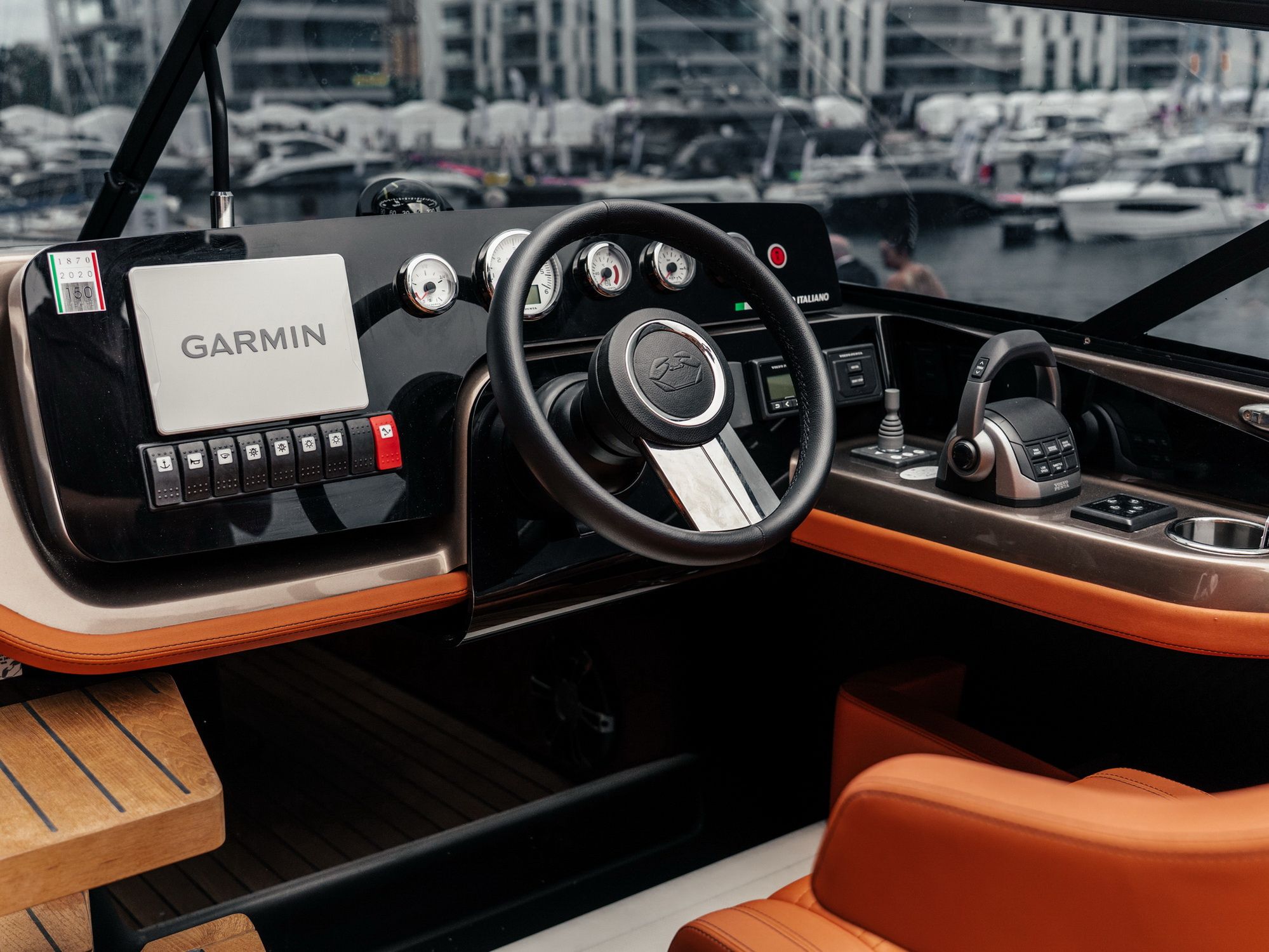 Sterówka jachtu Cranchi E26 Classic z pomarańczową tapicerką, kierownicą, wyświetlaczem Garmin i panelem kontrolnym w marinie.
