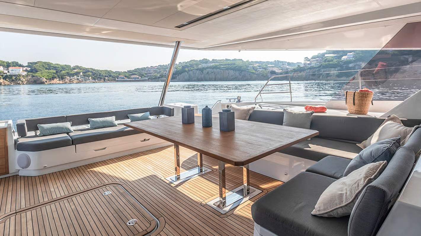 Duży stół i wygodne kanapy na pokładzie rufowym katamaranu Fountaine Pajot Samana 59, z widokiem na morze i wybrzeże.