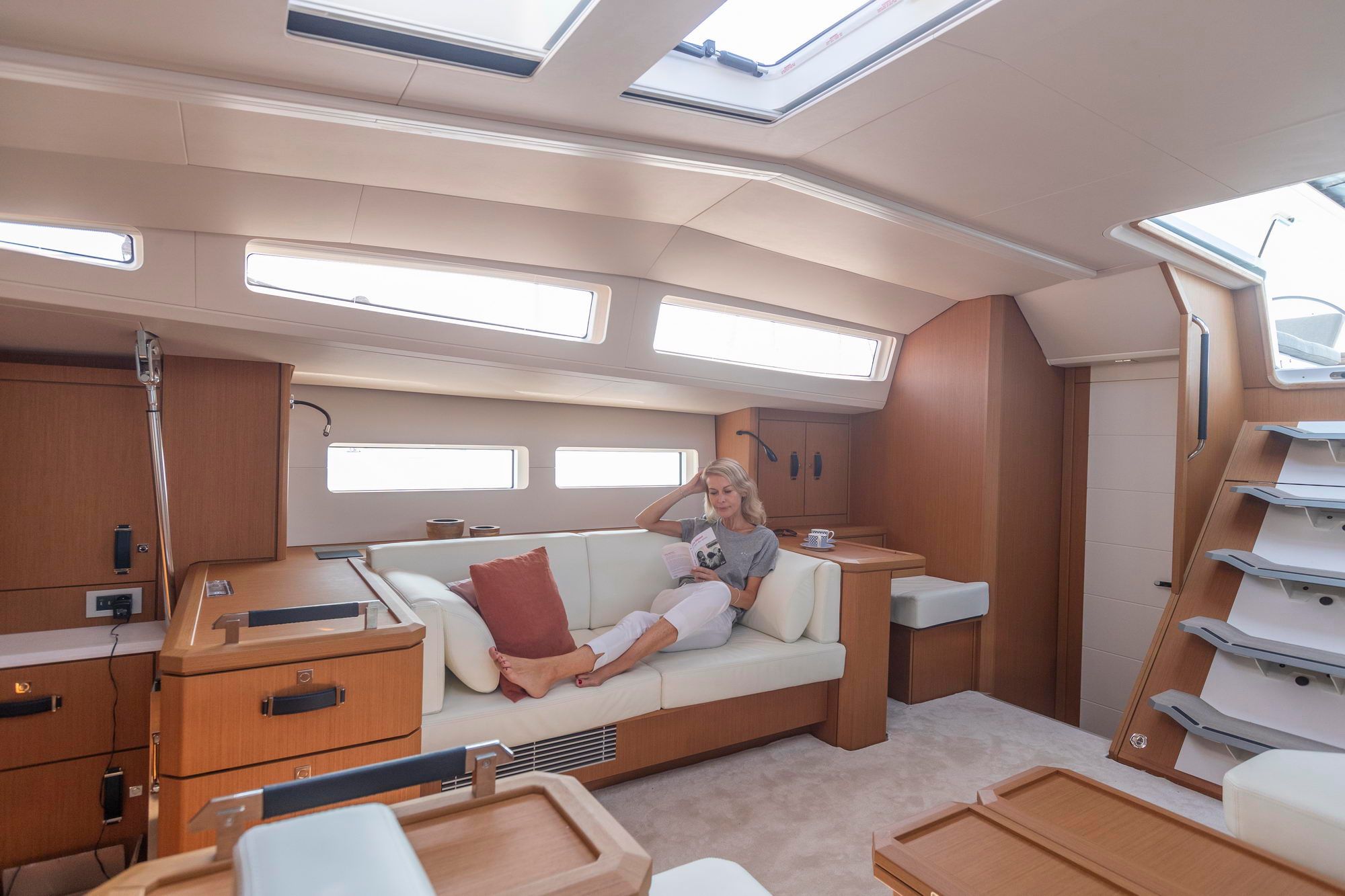 Kobieta odpoczywająca na sofie w salonie jachtu Jeanneau Yachts 60, widoczne drewniane meble i okna.