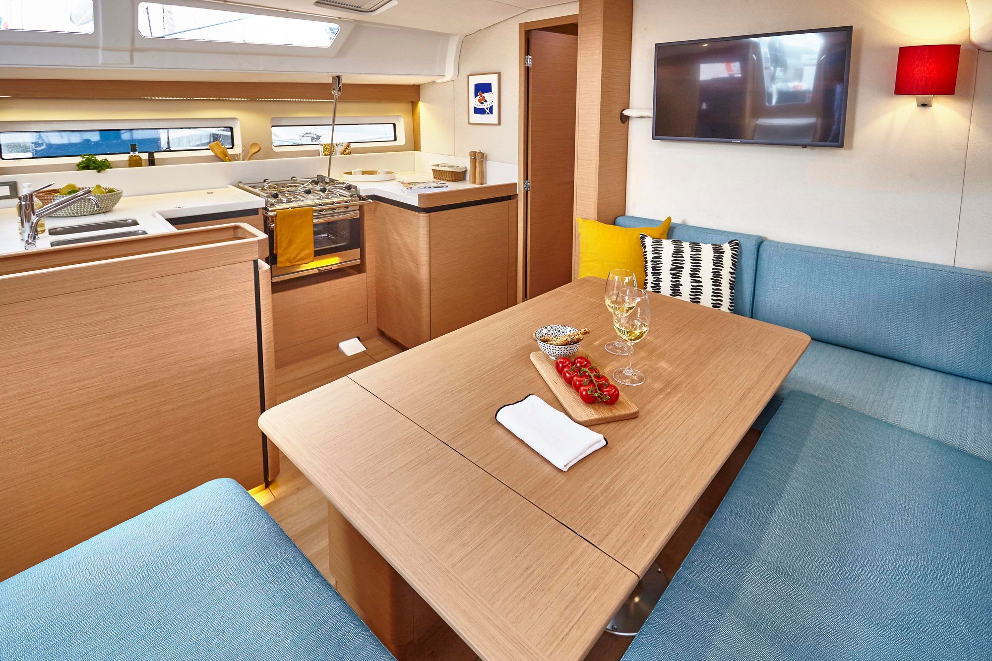 Interior of the Jeanneau Sun Odyssey 490 with saloon, table, sofas, TV and kitchenette.