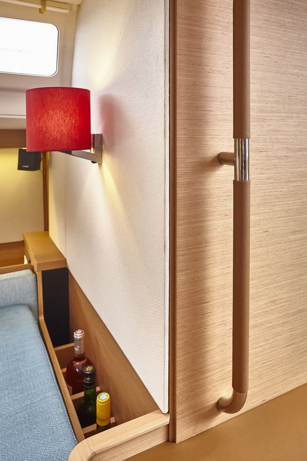 Wnętrze kabiny jachtu Jeanneau Sun Odyssey 490 z czerwoną lampą ścienną, drewnianymi panelami i schowkiem na butelki.