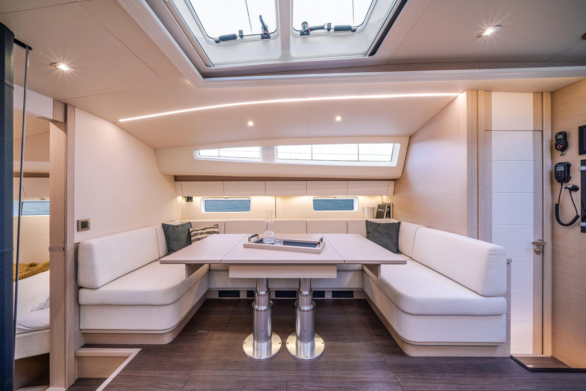 Przestronny salon jachtu Jeanneau Yachts 65 z jasnymi kanapami, regulowanym stołem i dużymi oknami zapewniającymi naturalne światło.