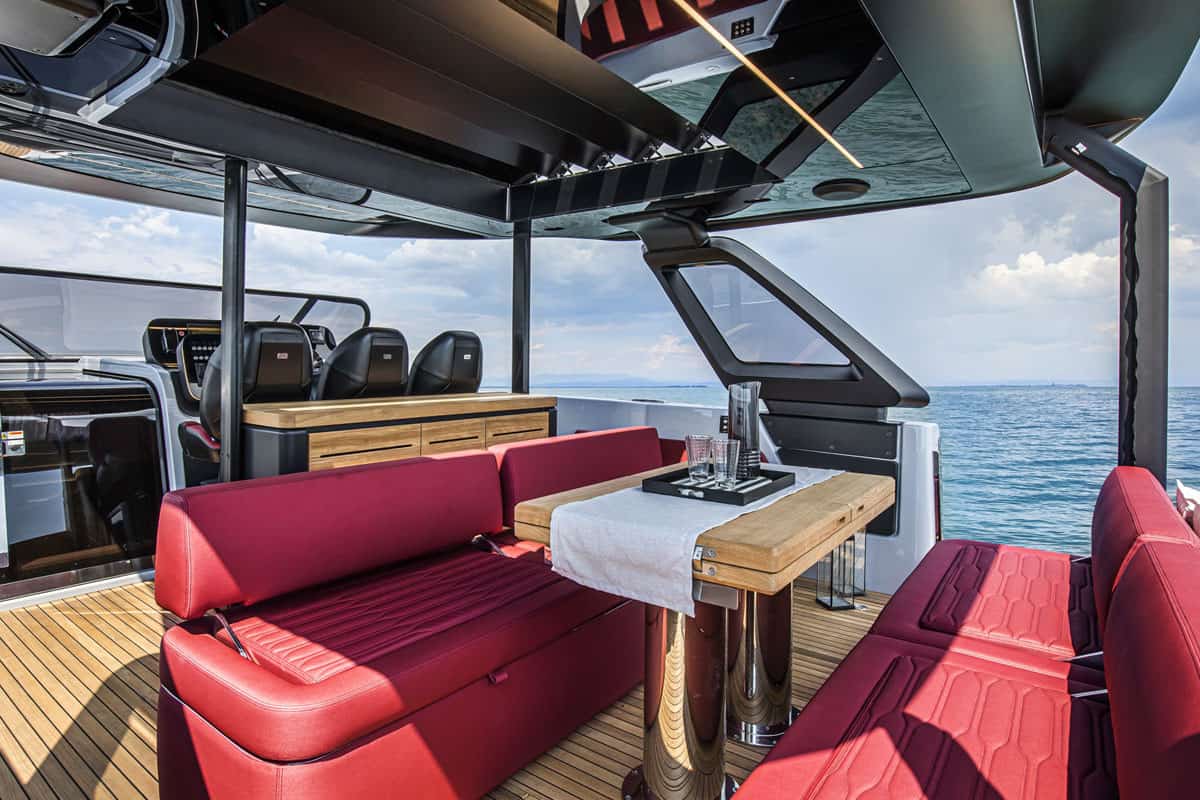View of the central deck area of the Cranchi A46 Luxury Tender with red sofas, wooden table and helm console in the background.