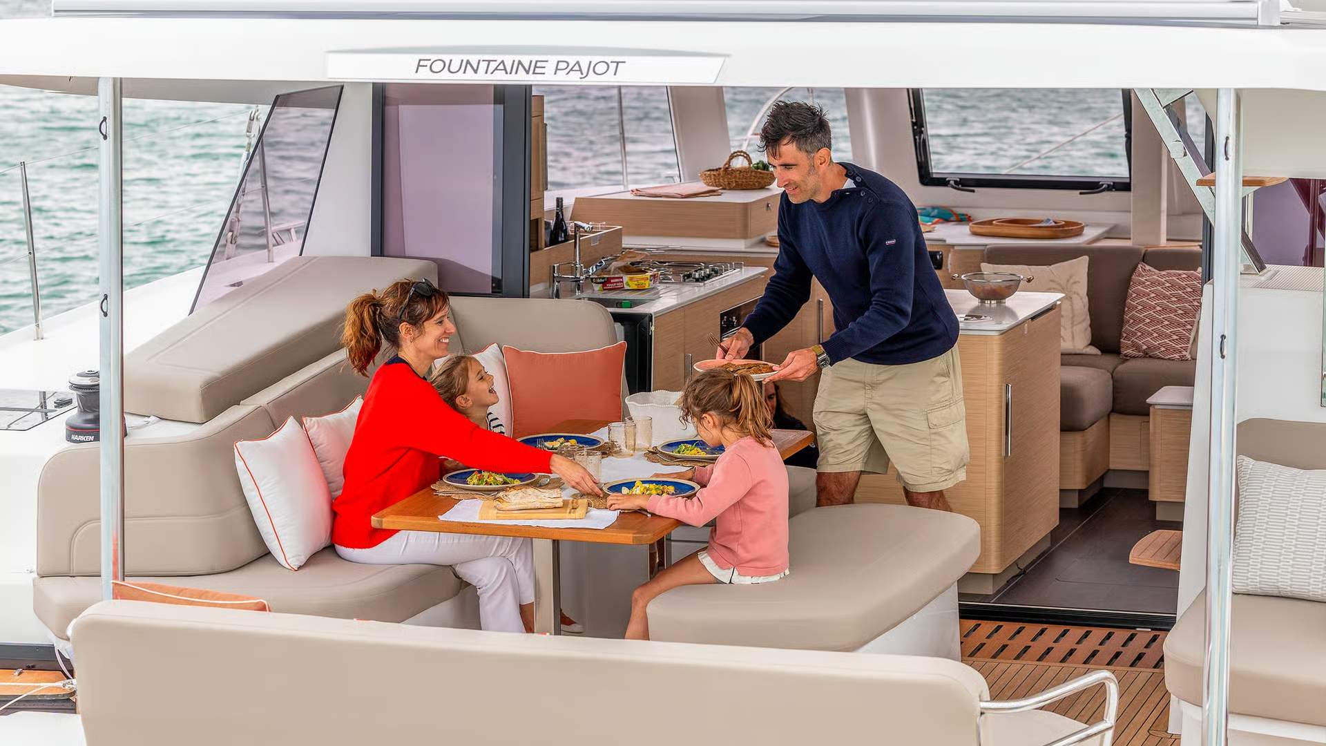 Eine Familie isst im großzügigen Cockpit an Bord des Katamarans Fountaine Pajot FP41, mit Meerblick und Teil der Kombüse.