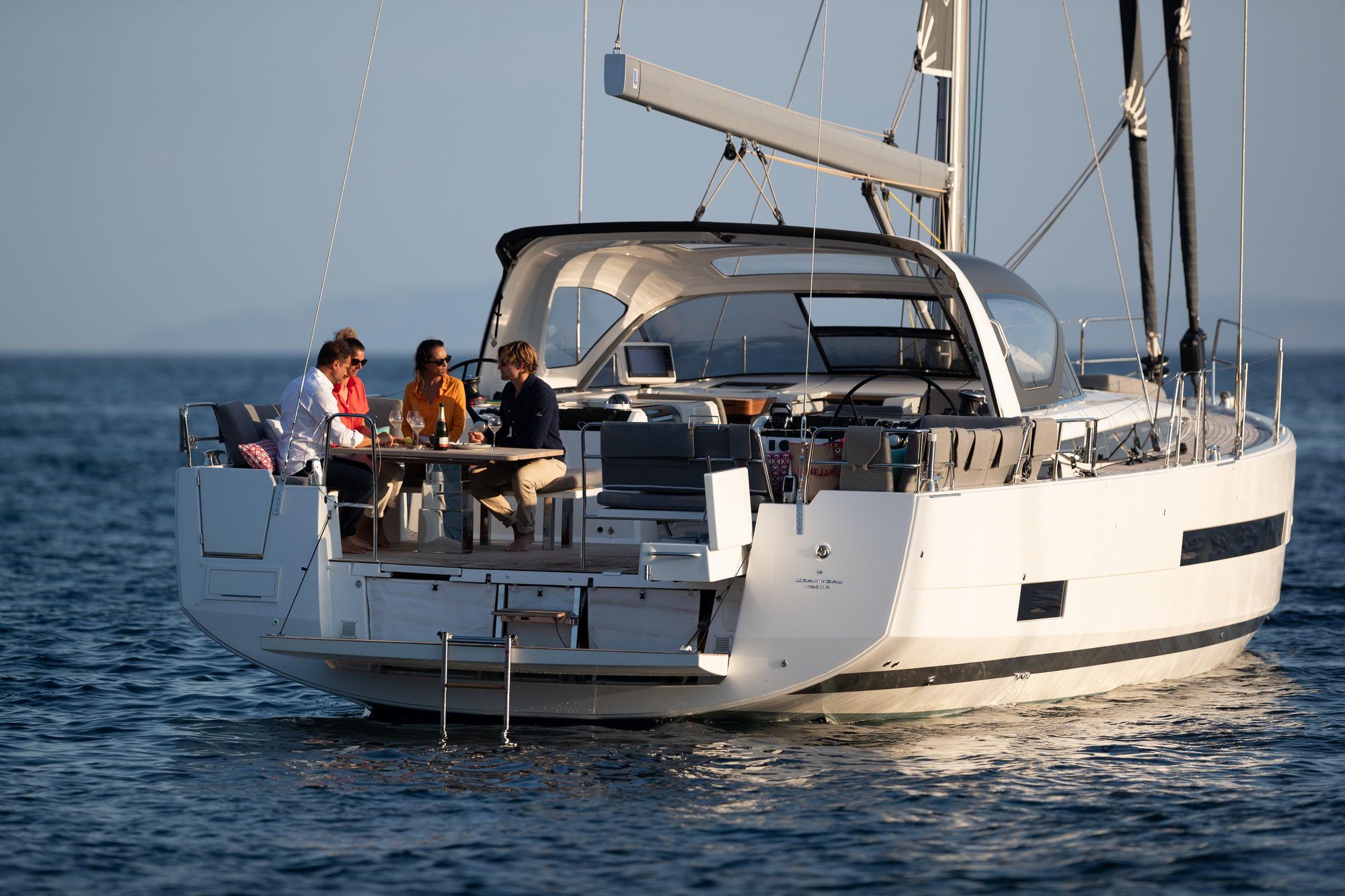 Cztery osoby siedzące przy stole w rufowym kokpicie jachtu żaglowego Jeanneau Yachts 55 na wodzie.