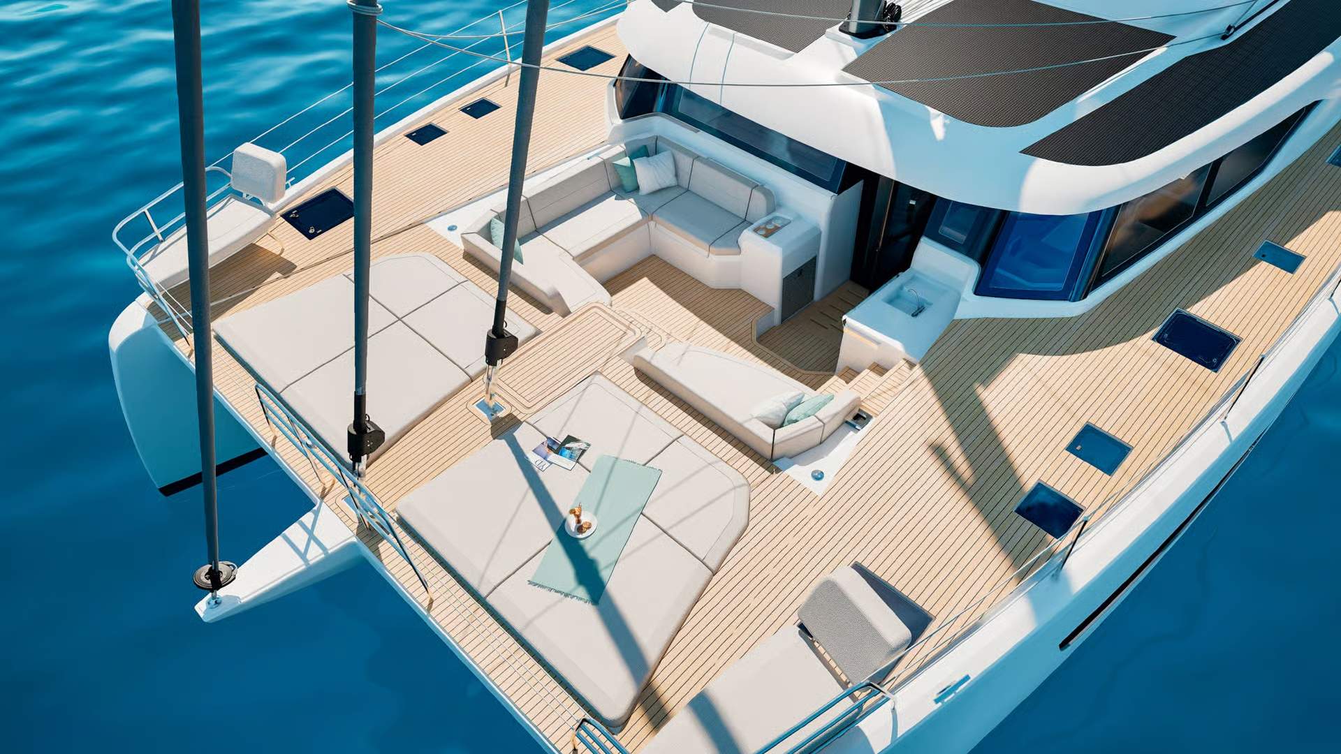 Widok z góry na kokpit dziobowy i pokład słoneczny katamaranu Fountaine Pajot FP55 na tle błękitnej wody.