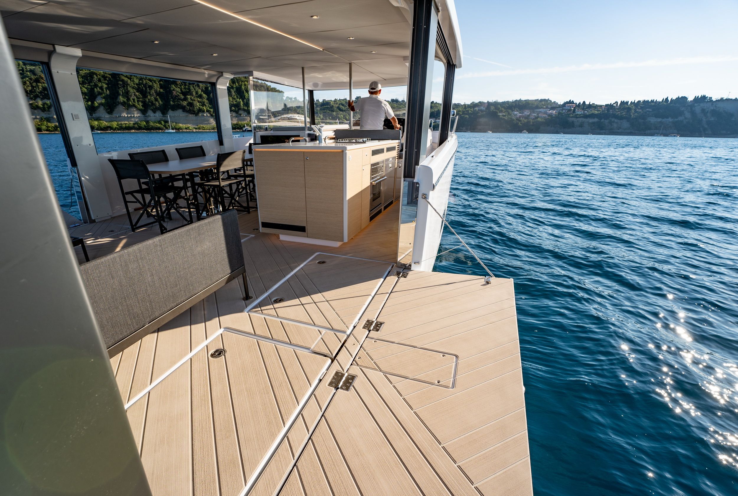 Offenes Achterdeck der Jeanneau Sea Loft 480 mit ausklappbarer Plattform, Esstisch und sichtbarem Steuermann.