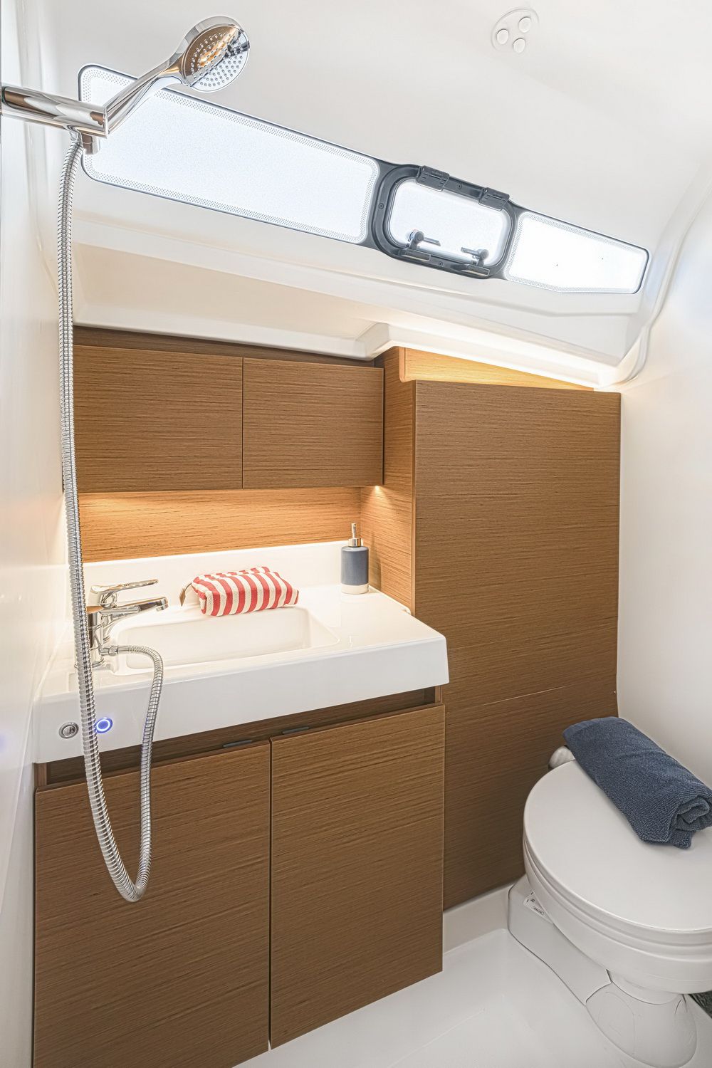 Modernes Badezimmer auf der Segelyacht Jeanneau Sun Odyssey 380 mit Waschbecken, Dusche, Toilette und Holzschränken.