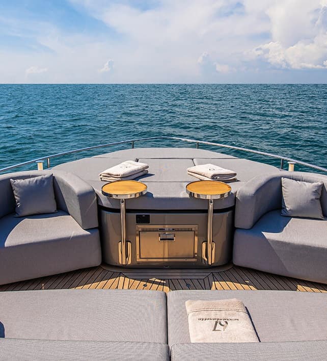 Widok na otwarty salon dziobowy jachtu Cranchi Sessantasette 67 z sofami, stolikami i mini-lodówką, na tle morza.