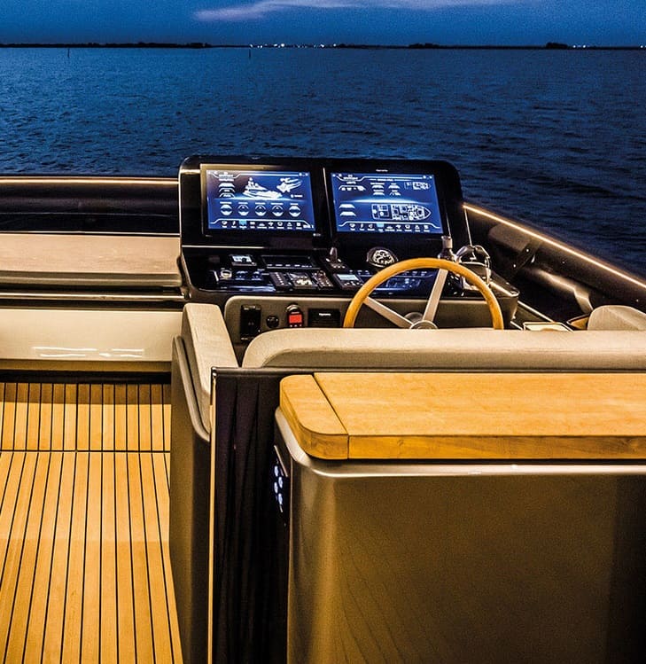 Helm station of the Cranchi Sessantasette 67 with two navigation displays and a wooden wheel, sea view.