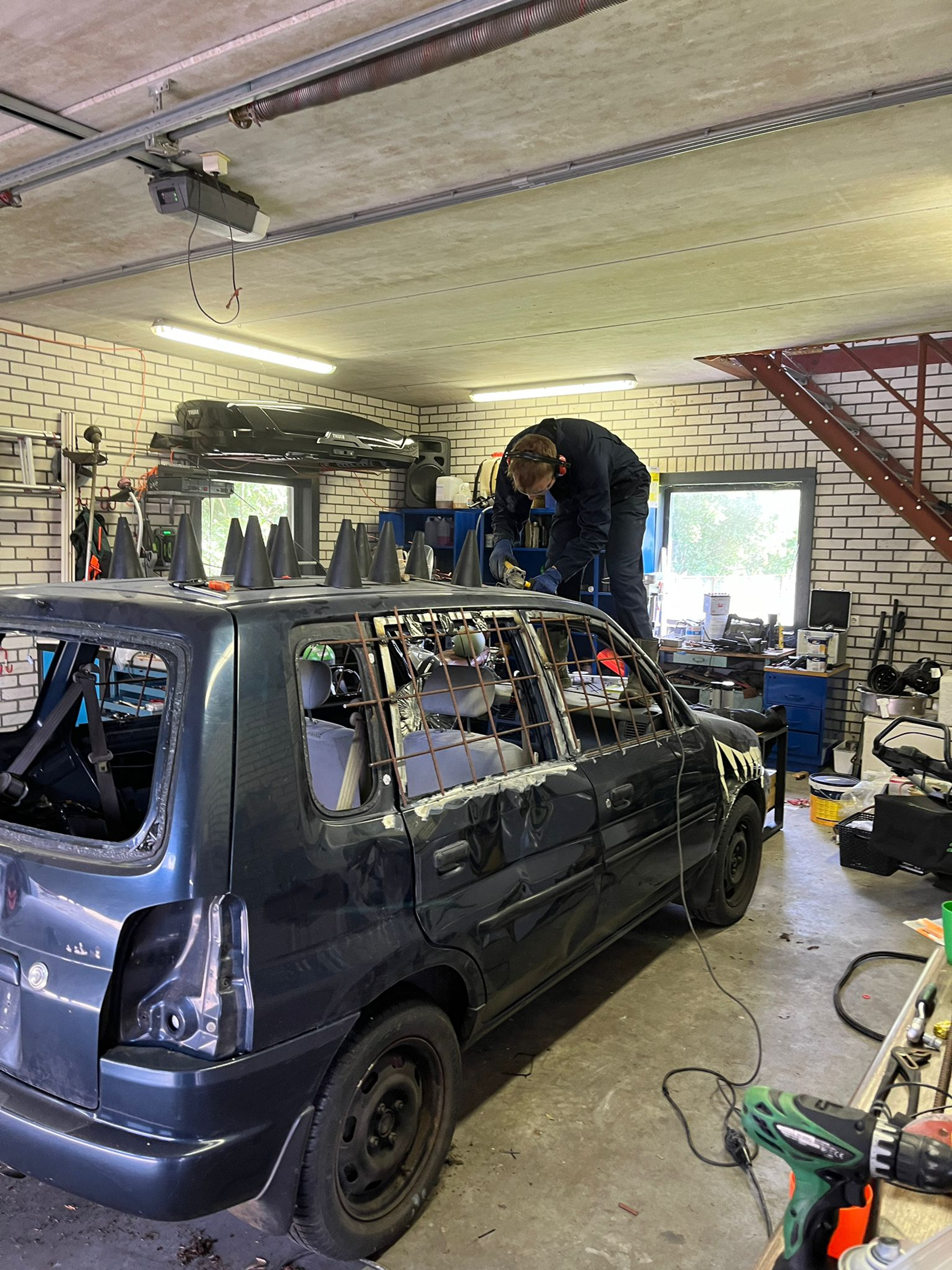 Een auto wordt in een garage omgebouwd voor autocross, met tralies voor de ramen en pionnen op het dak