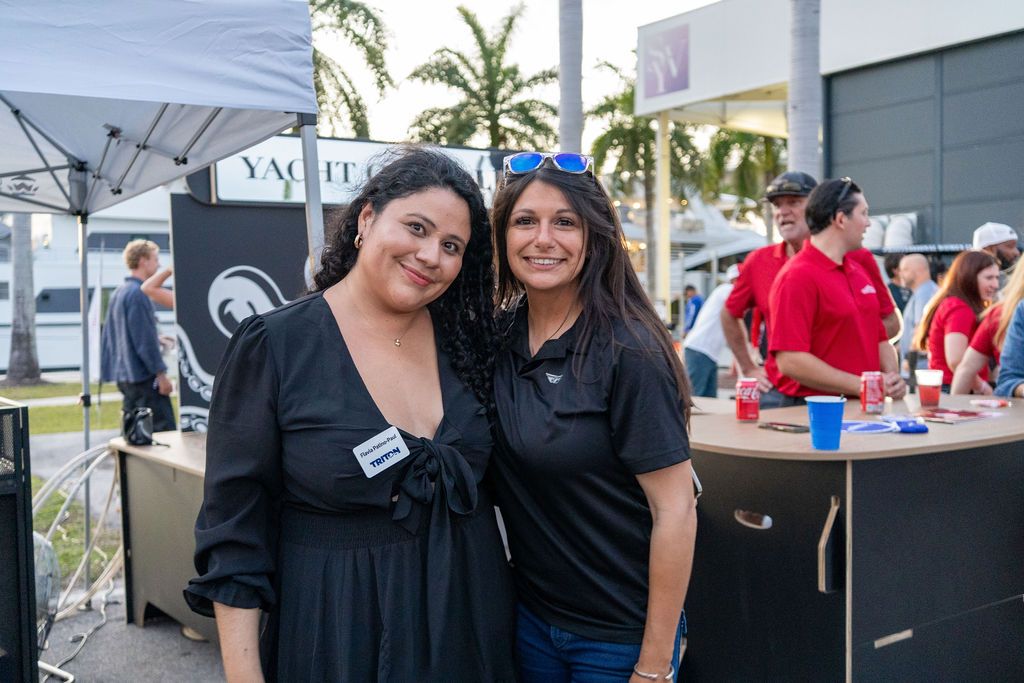 Two attendees at the April 2026 Triton Expo with exhibitor booths behind them