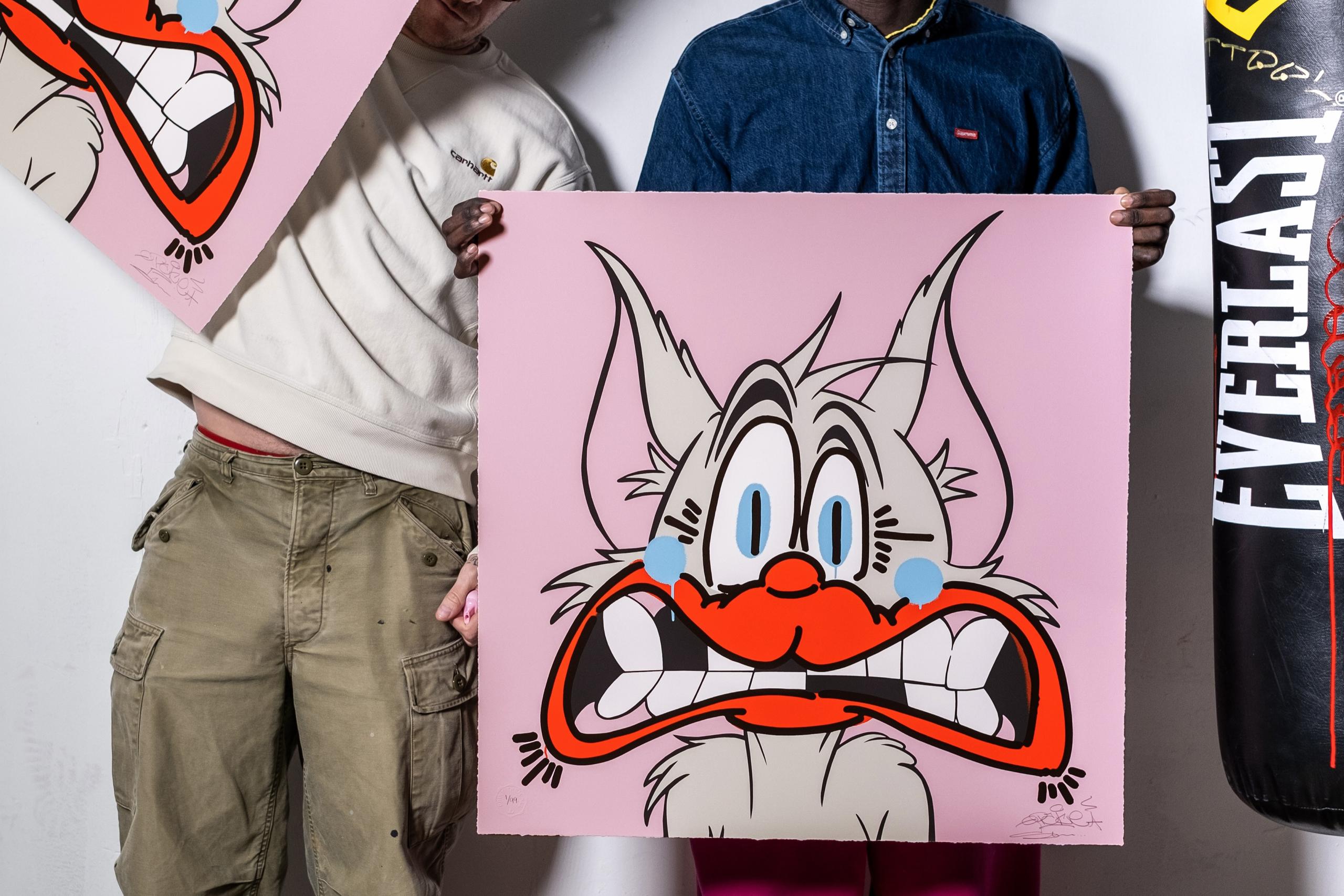 Two men stand in a studio holding large pink artworks featuring an