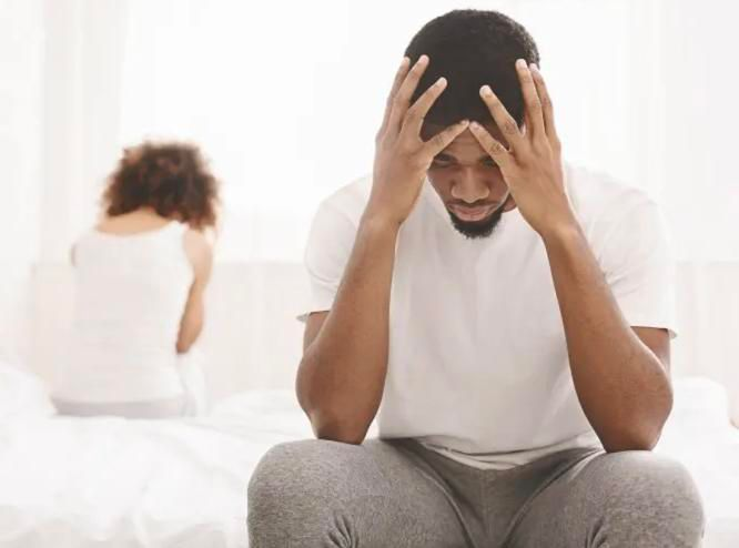 man looking distressed with hands on his head while woman is sitting on the other side of the bed