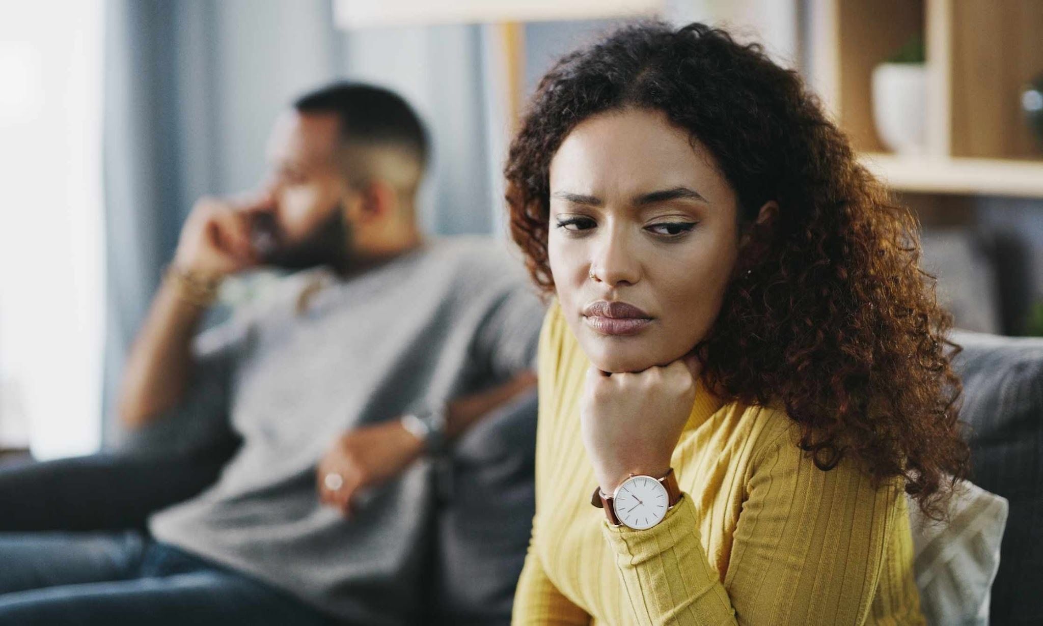 african ethnicity woman sitting and thinking while white man in the background doing something