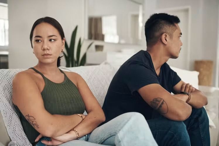 Asian woman and man sitting on a couch while looking separate ways likely after an argument